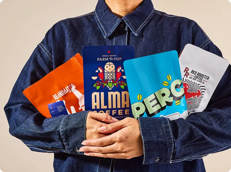 Closeup of a woman in a jean jacket holding 4 different bags of coffee in her arms.