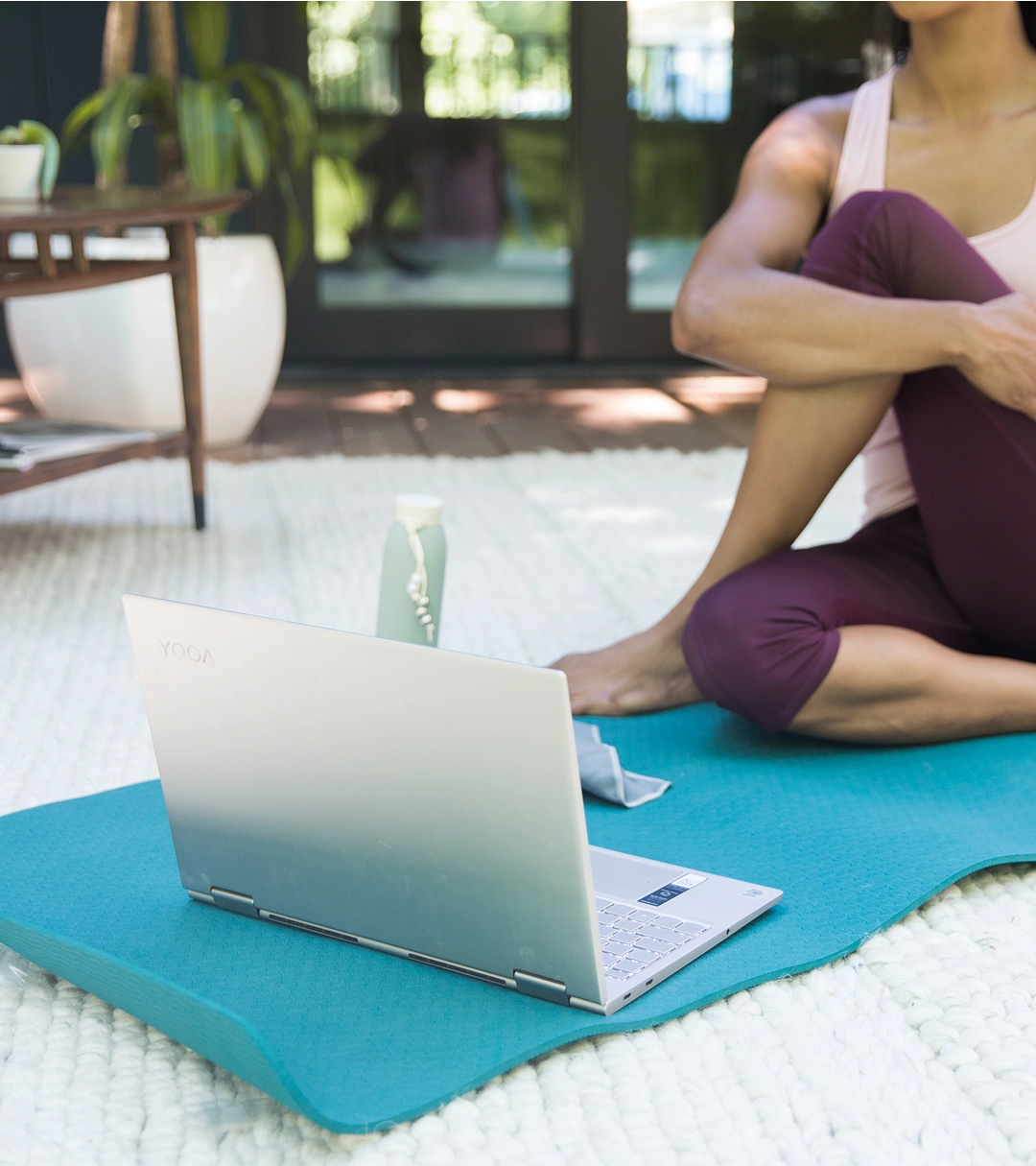 Person sitting on a yoga mat with a laptop and water bottle.