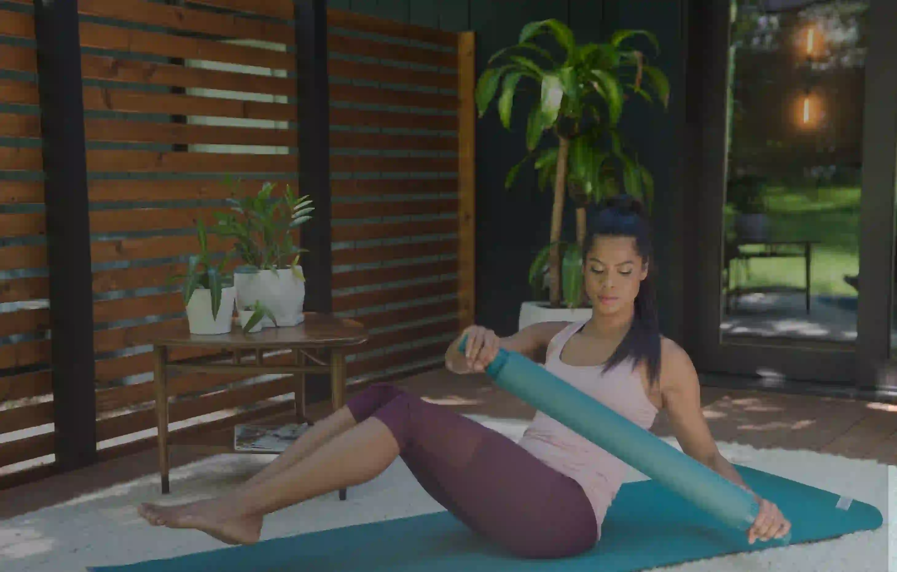 Woman sitting on a yoga mat holding a foam roller indoors.