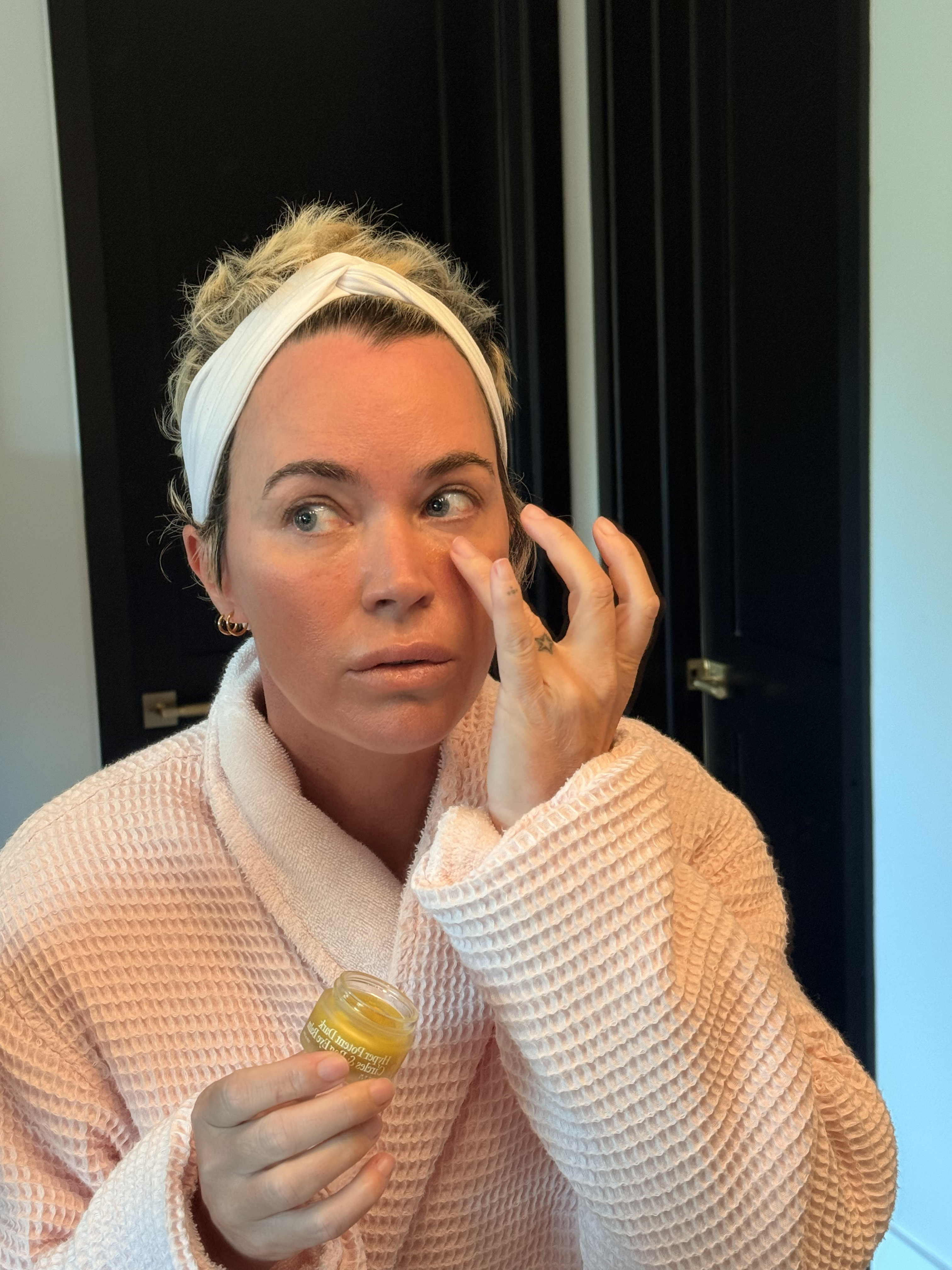 Person applying cream to face with a small jar in hand.