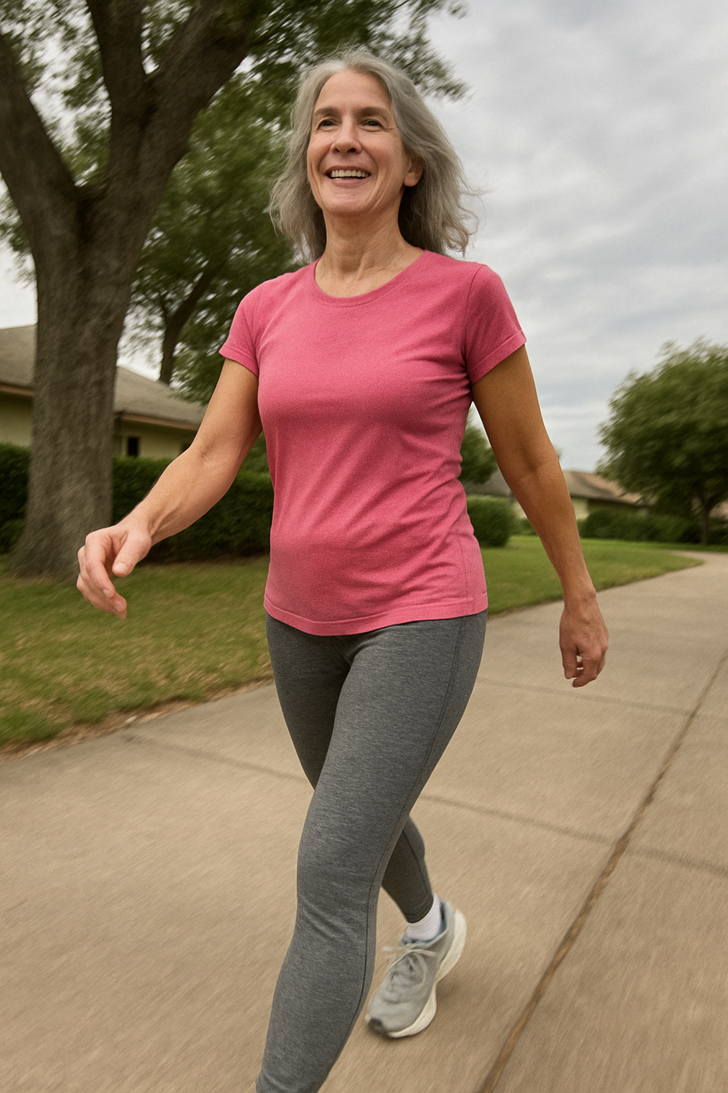 Woman in pink shirt walking on a sidewalk, smiling.