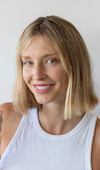 Person with short blonde hair smiling against a plain background.