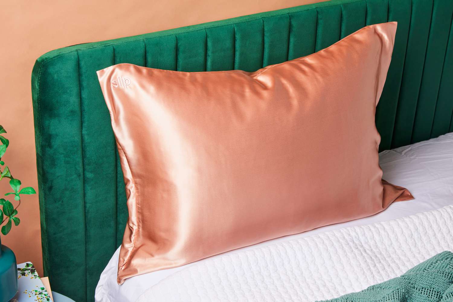 Peach silk pillow on a green velvet headboard bed.