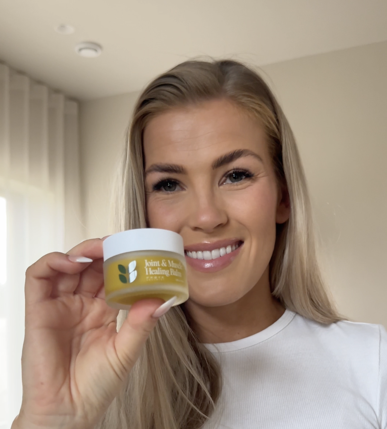 Person holding a jar of Joint & Muscle Healing Balm, smiling at the camera.