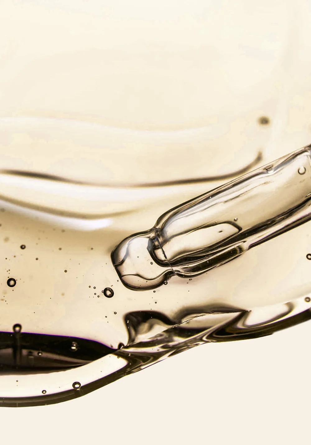 A close-up macro shot of a glass dropper submerged in a clear, yellowish, viscous liquid with bubbles.