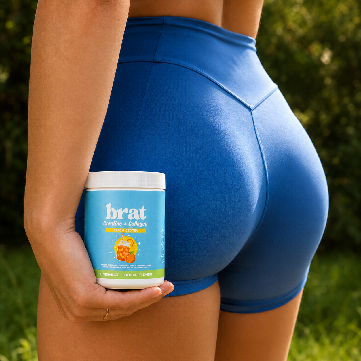 A woman in blue shorts, seen from behind, holds a container of Brat Creatine + Collagen supplement.