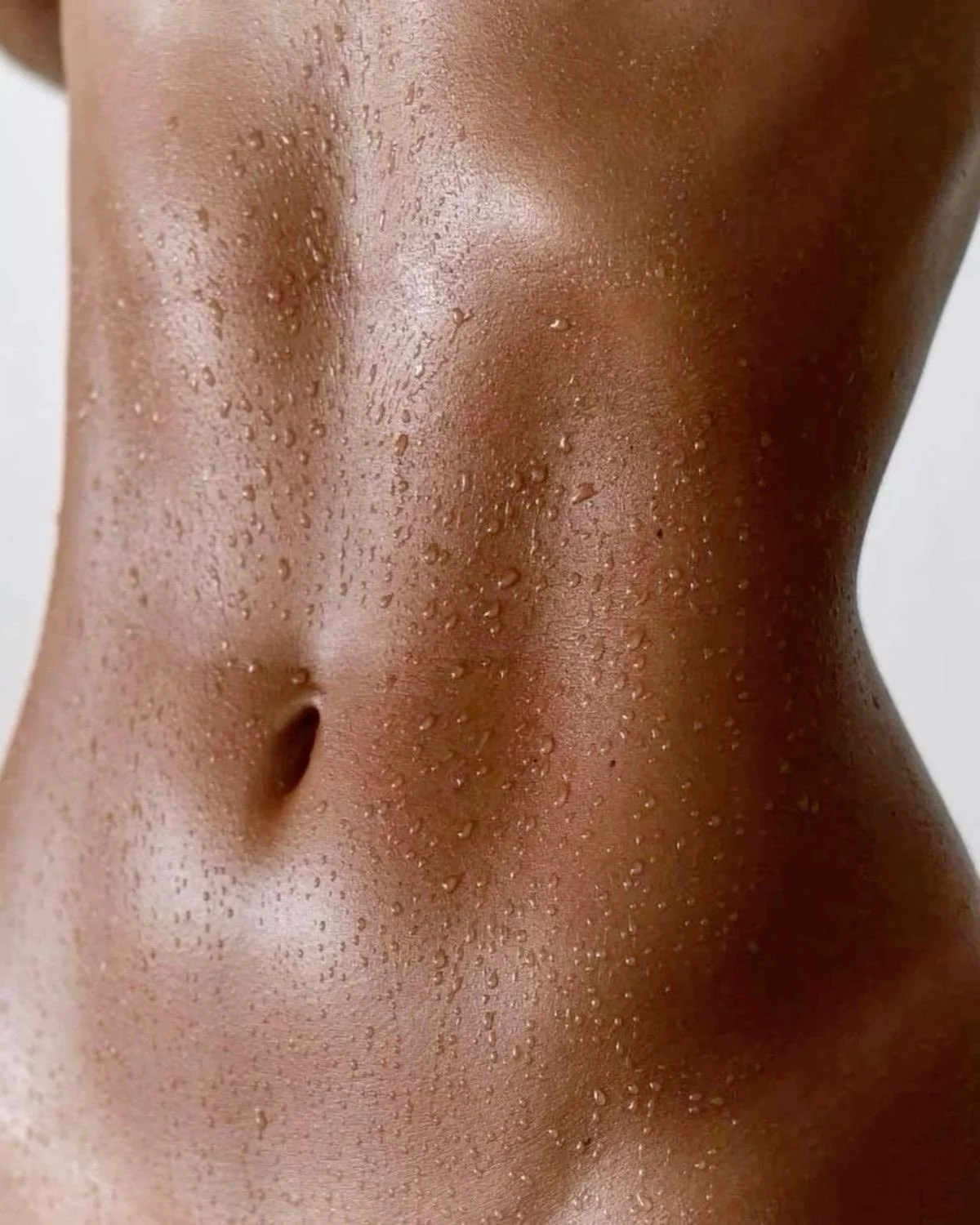 A close-up of a person's toned midsection covered in small droplets of water.