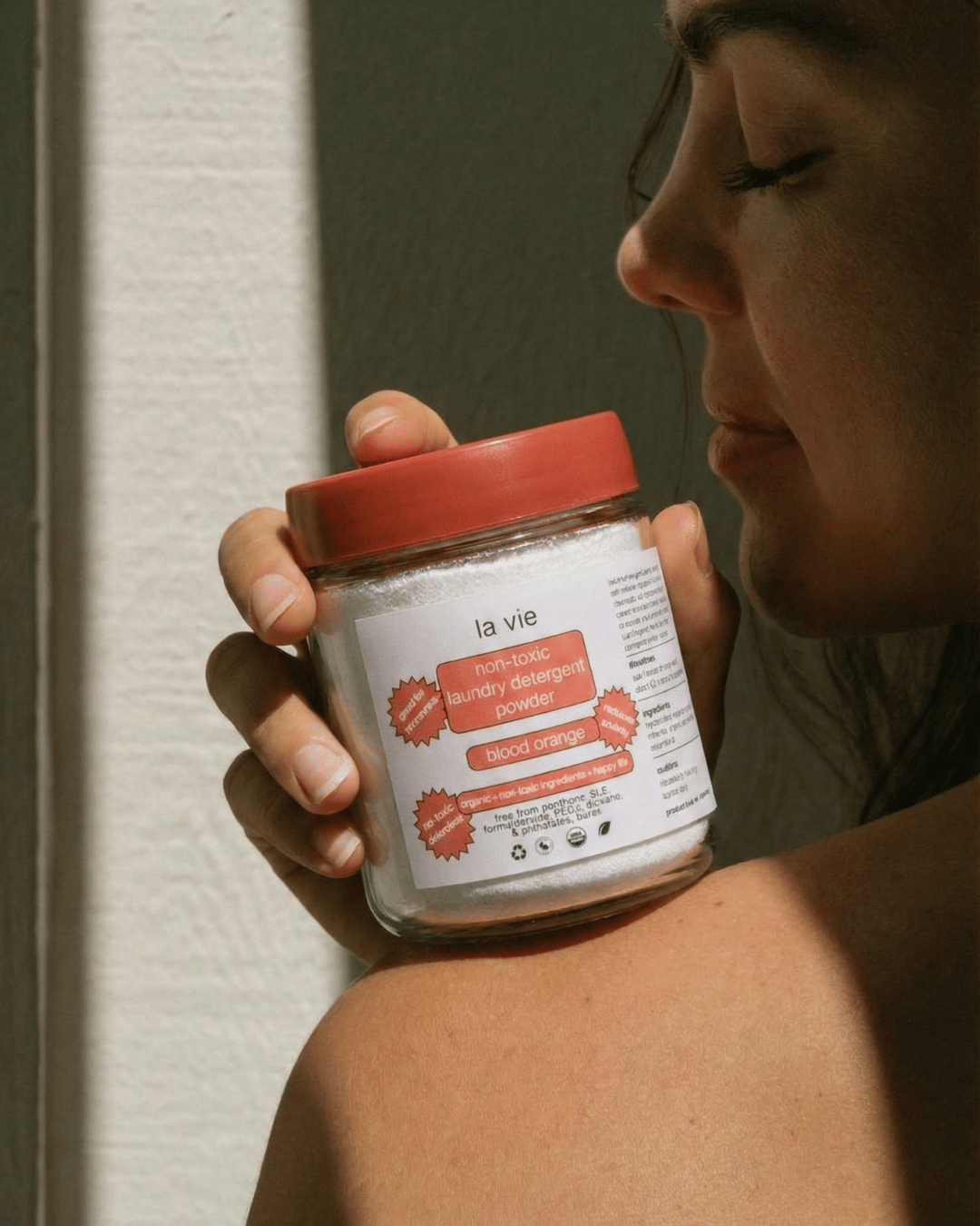 Person holding a jar of blood orange laundry detergent powder.