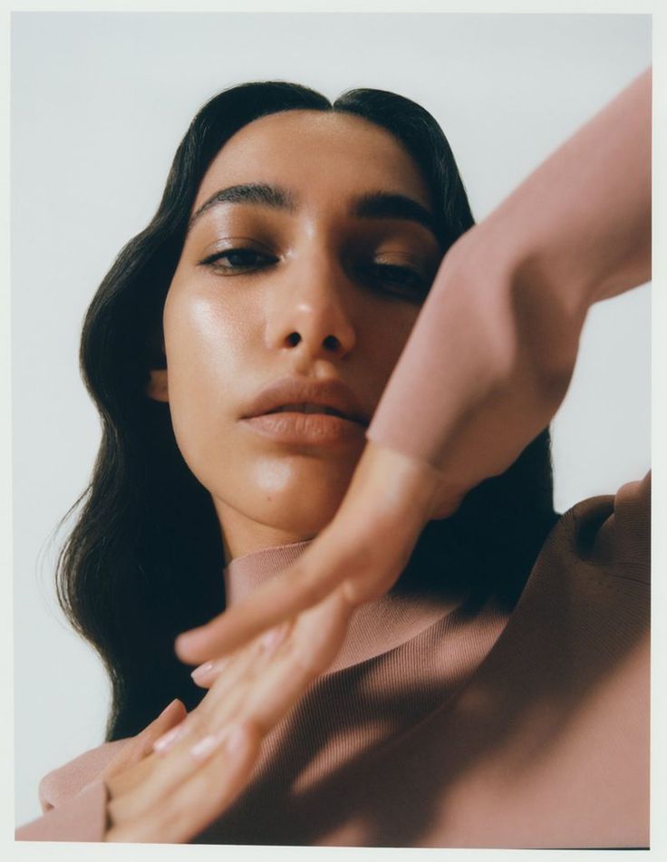 Close-up of a person with long hair, hand raised, wearing a pink top.