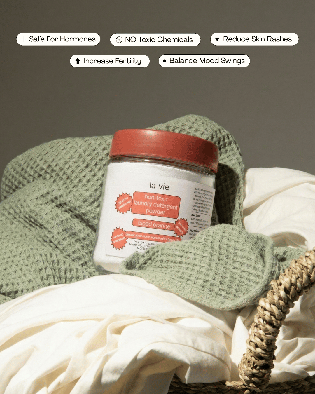 Jar of non-toxic laundry detergent on folded fabrics in a basket.