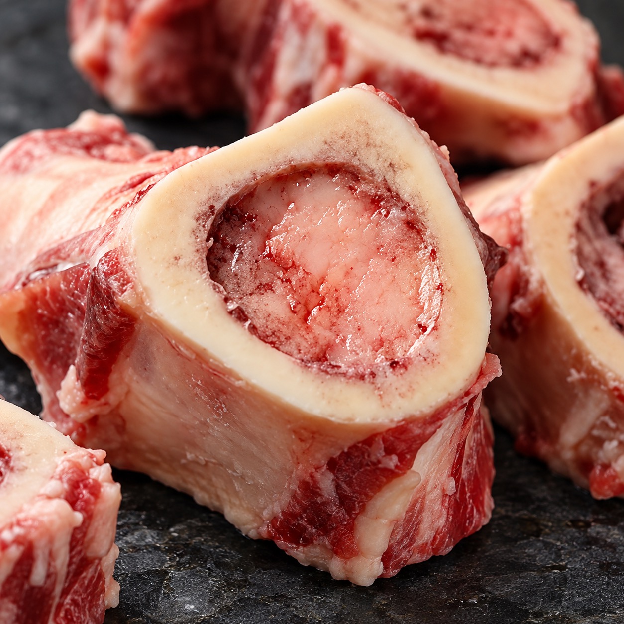 A close-up of several raw, cross-cut beef marrow bones on a dark slab.