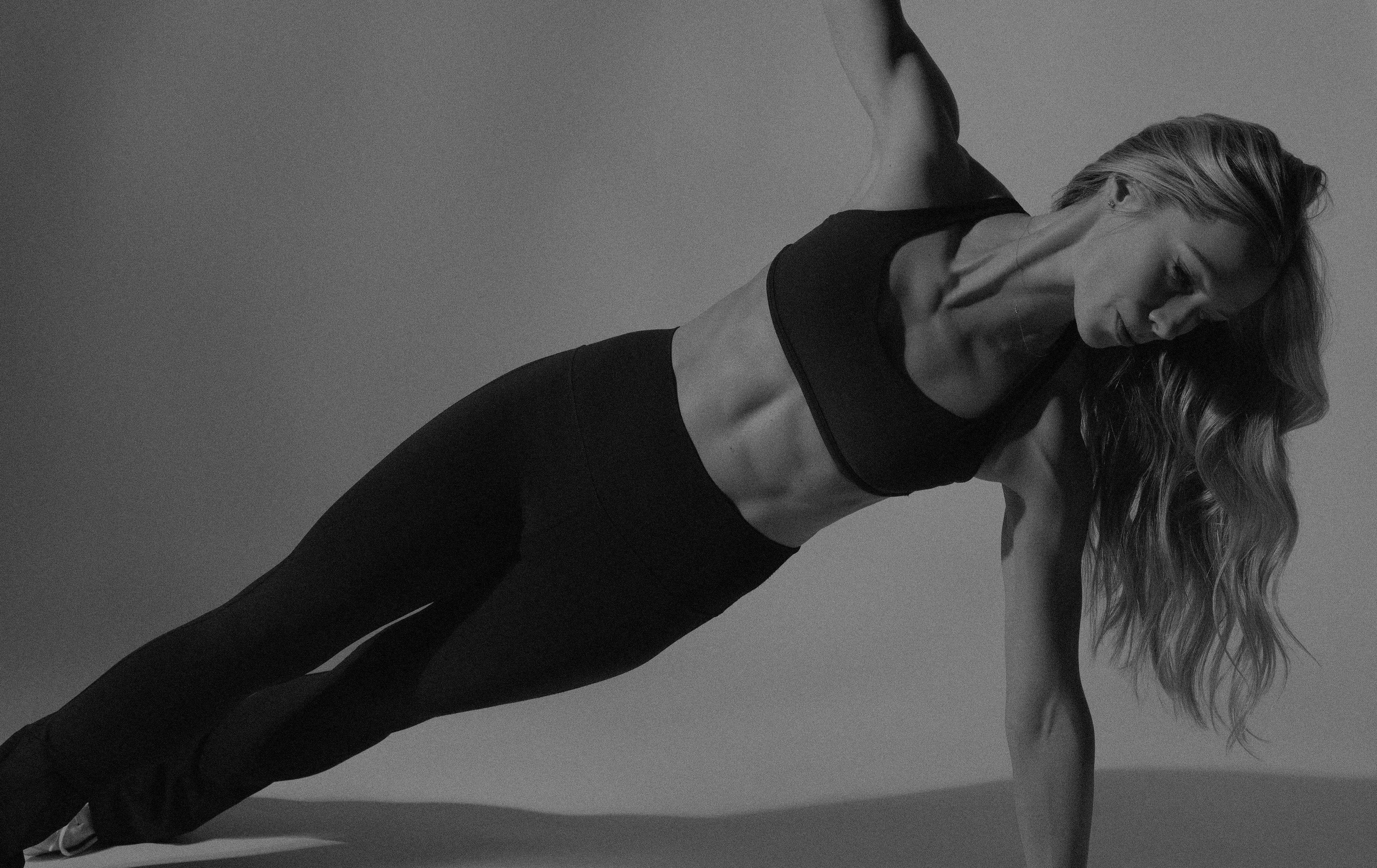 Black and white image of a woman in a side plank position.