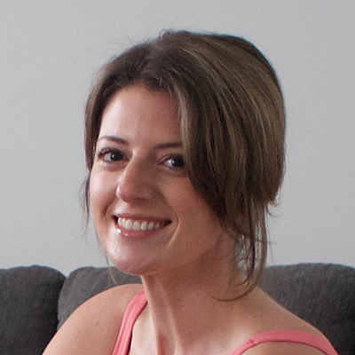 A headshot of a smiling woman with brown hair and a pink top, sitting on a couch.