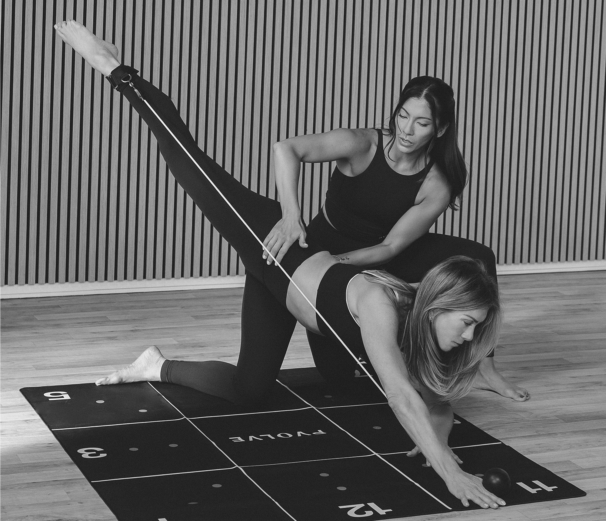 Two women practicing yoga on a grid mat.