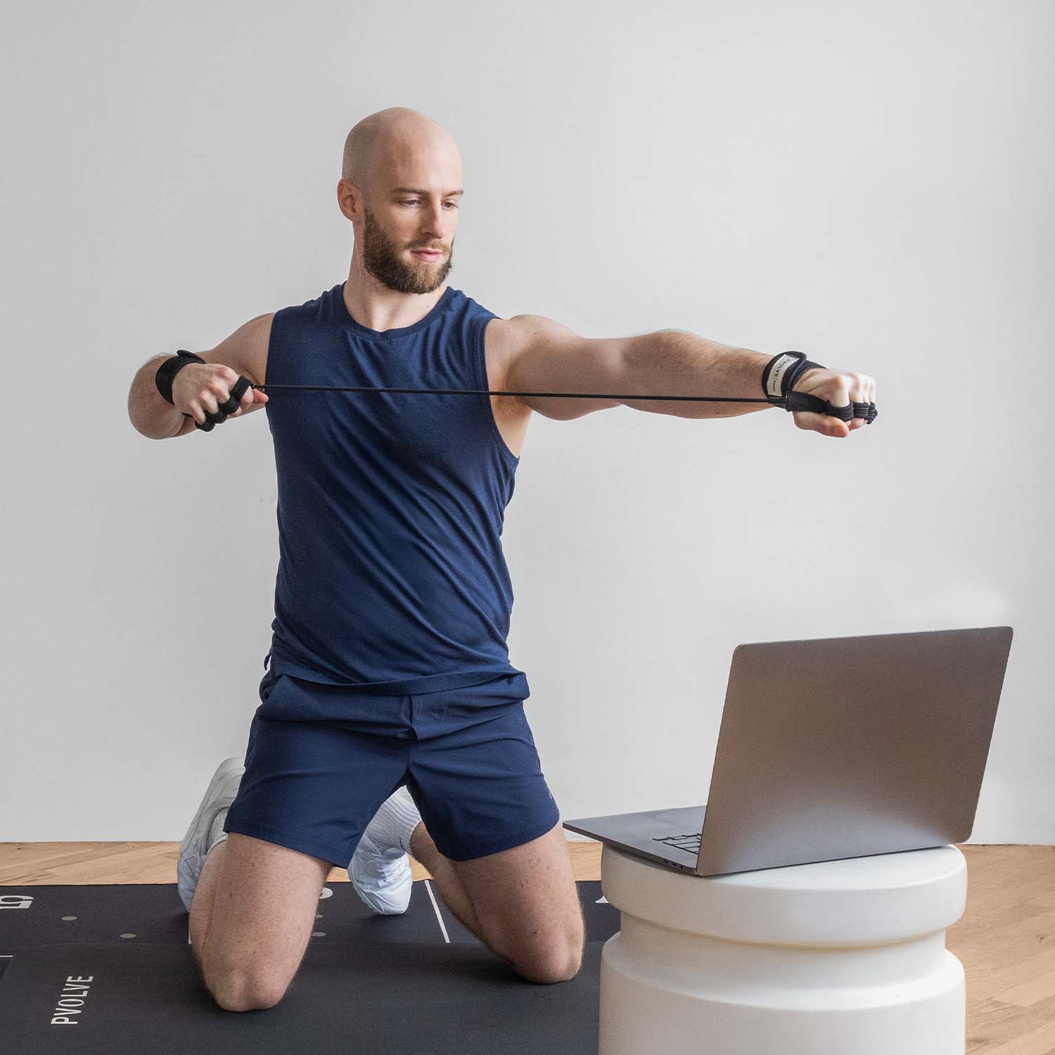 Man exercising with resistance band in front of a laptop.