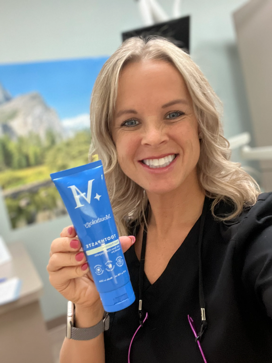 Person smiling and holding a blue toothpaste tube.