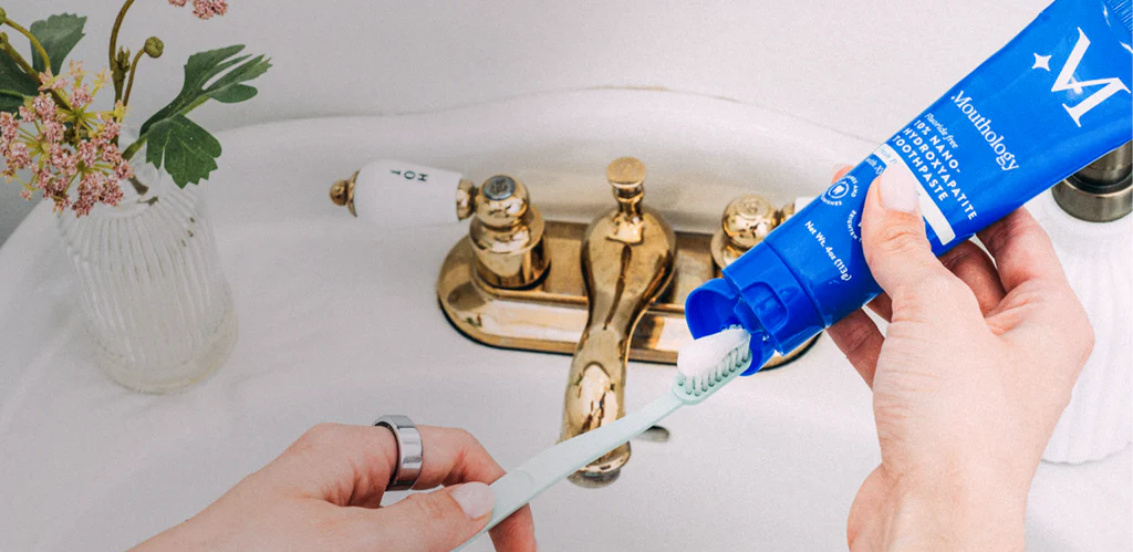 Person applying toothpaste to a toothbrush over a sink with flowers.