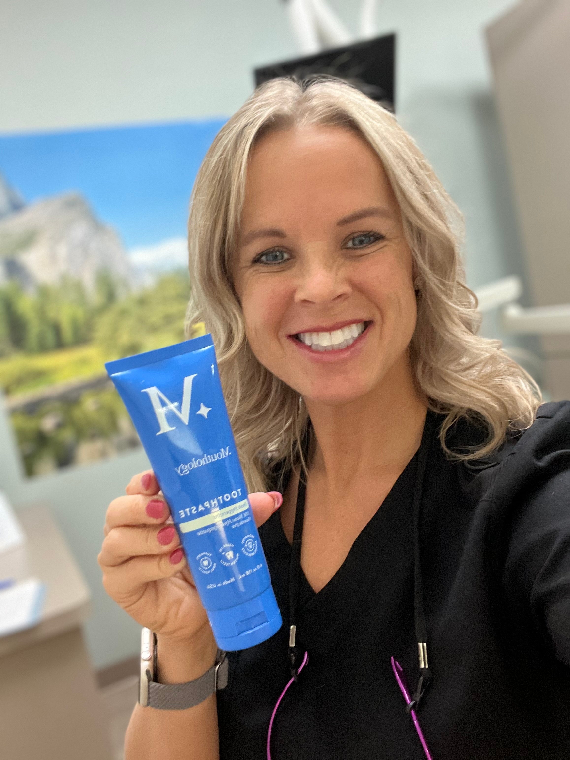 Person smiling and holding a blue tube of toothpaste.