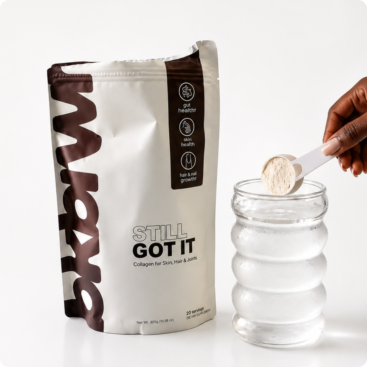 A hand holds a scoop of collagen powder over a glass of water, next to its packaging.