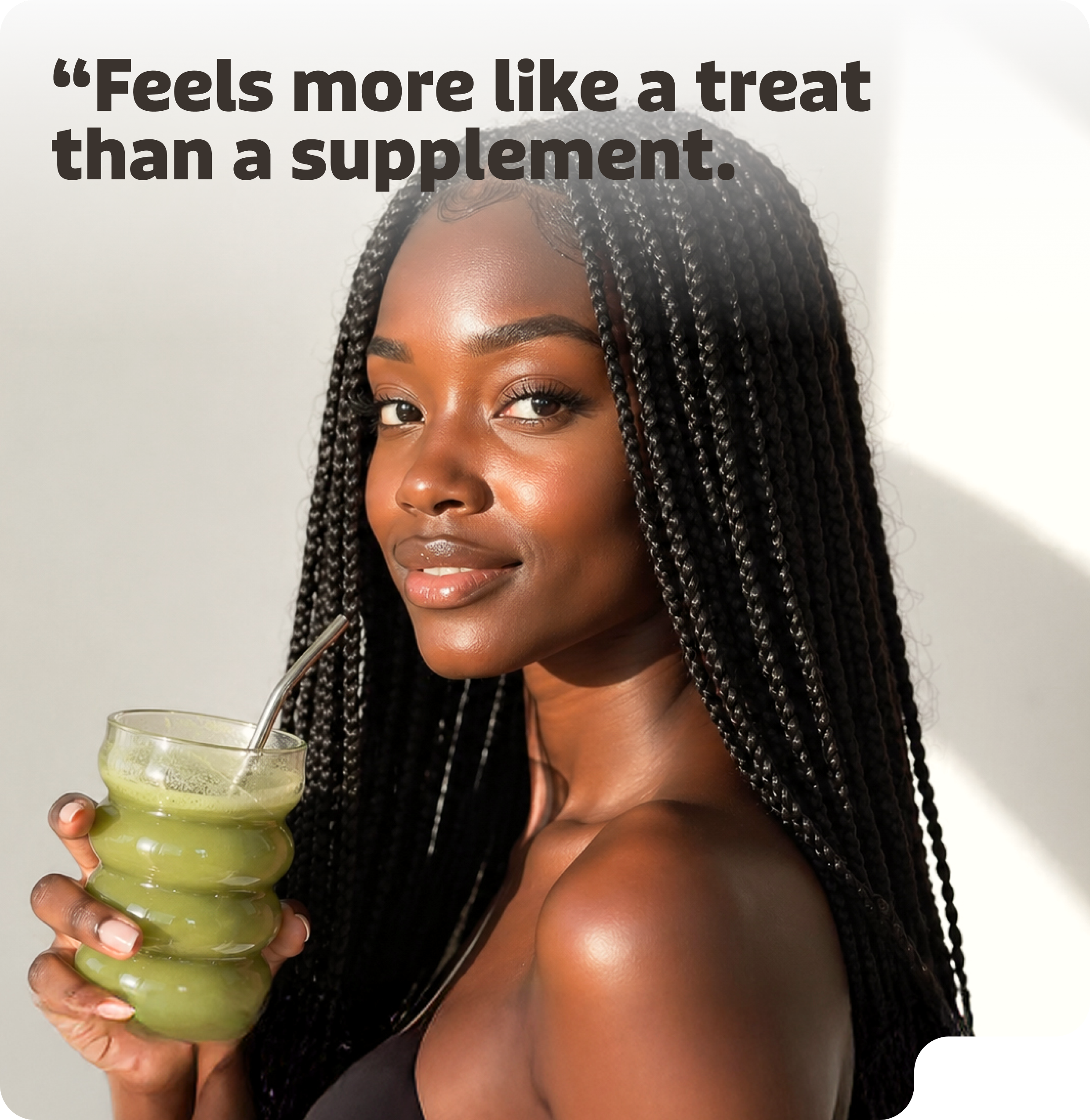 A woman with long braids smiles while holding a glass containing a green drink and a metal straw.
