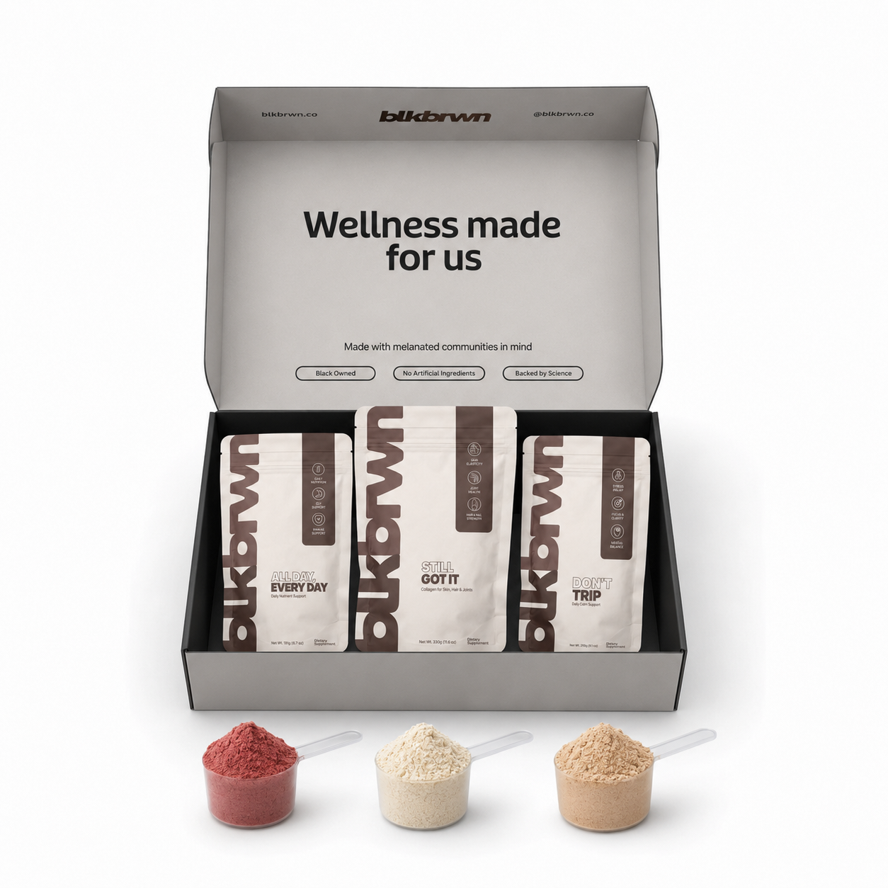 An open blkbrwn wellness box with three supplement pouches and three scoops of different colored powders in front.
