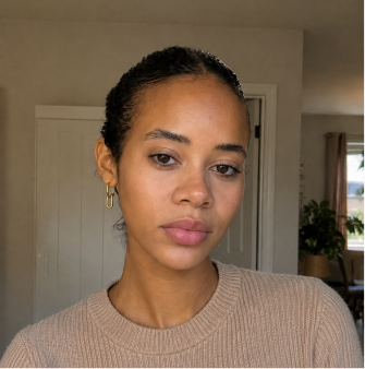 A woman with dark hair pulled back wearing a tan sweater and gold hoop earrings looks at the camera.