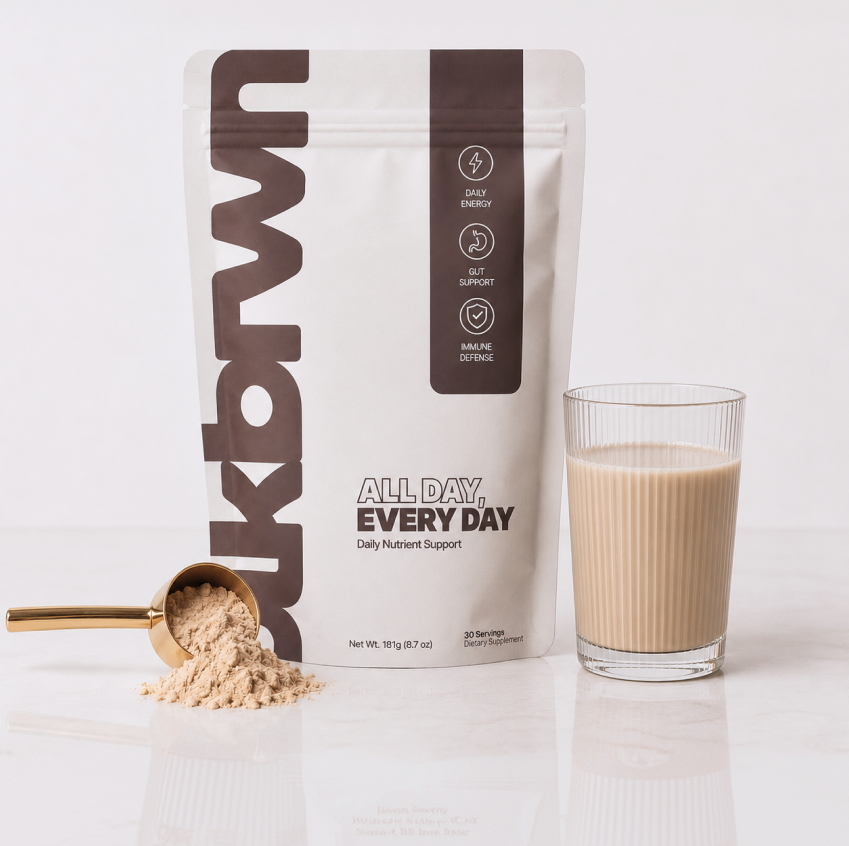 A bag of ukbrwn supplement powder sits next to a scoop of the powder and a prepared drink.