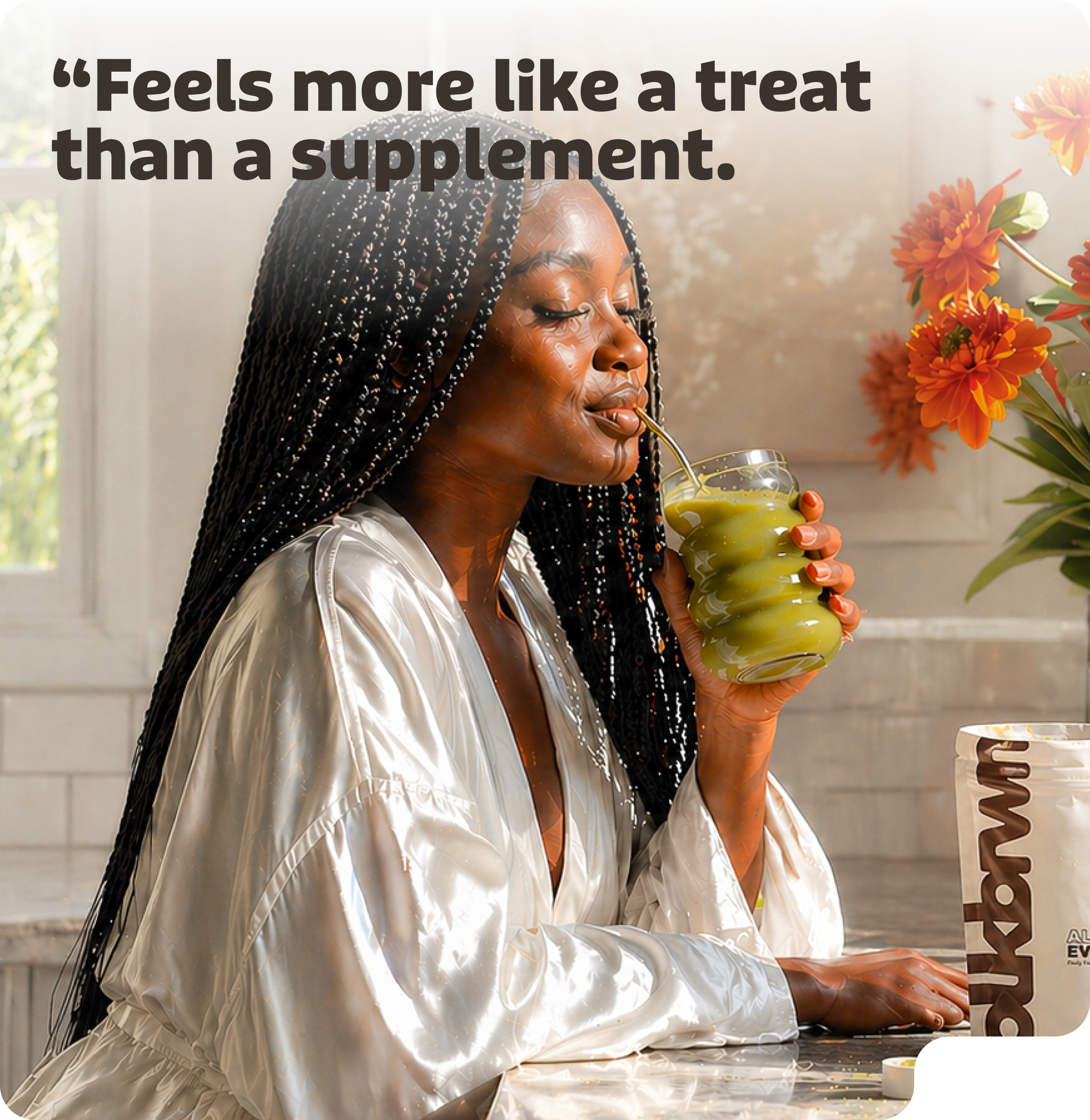 A woman with long braids in a white satin robe sips a green drink from a glass.
