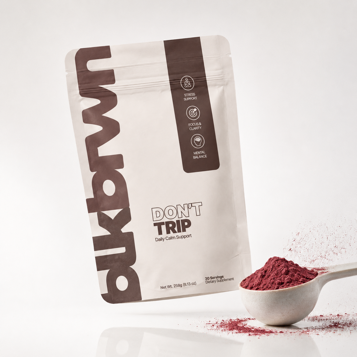 A pouch of Bukdwn Don't Trip supplement next to a scoop of red powder against a white background.