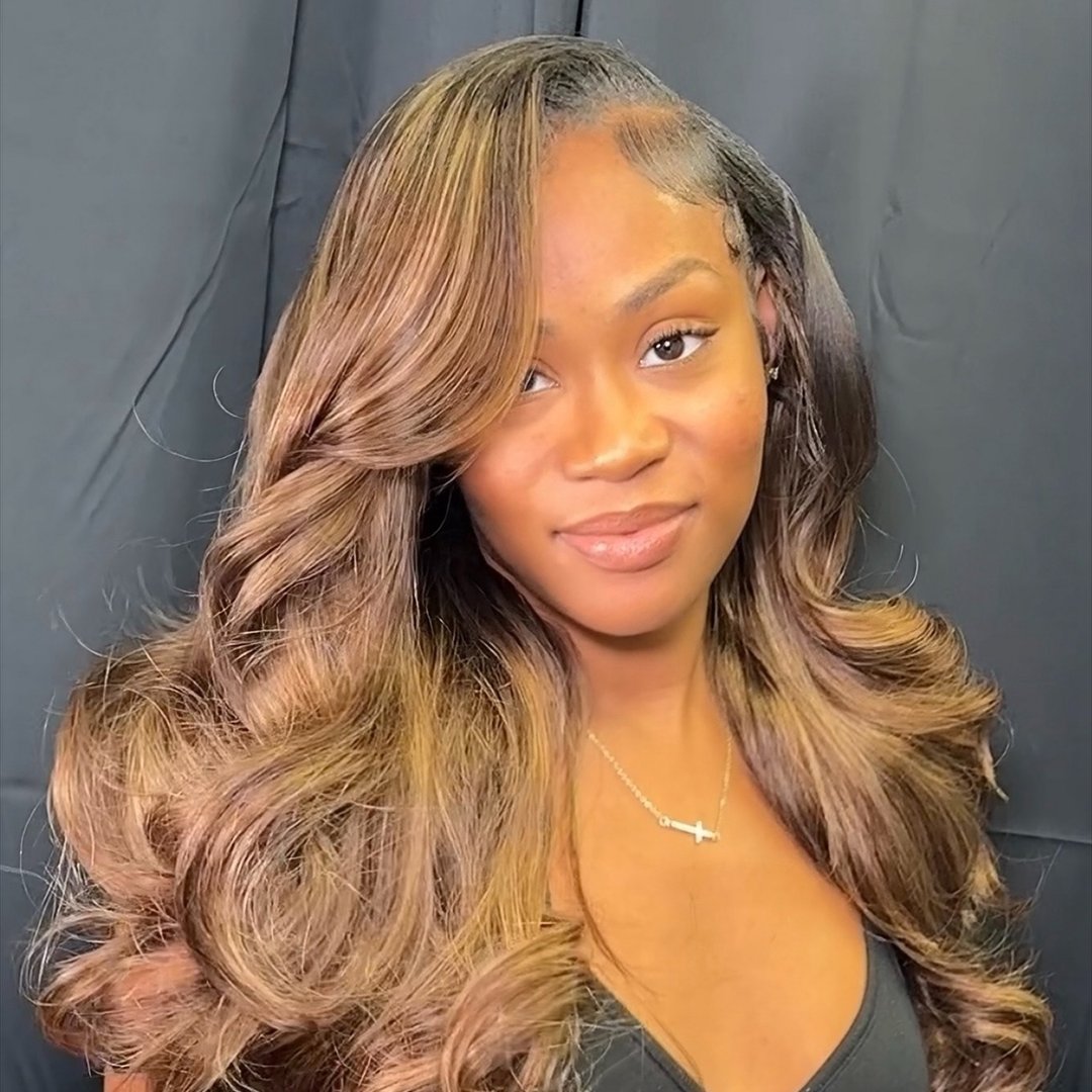 A woman with long, voluminous, wavy brown hair with blonde highlights, styled in a side part.