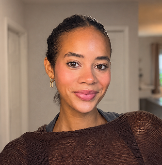 A woman with her hair braided and pulled back smiles gently at the camera.