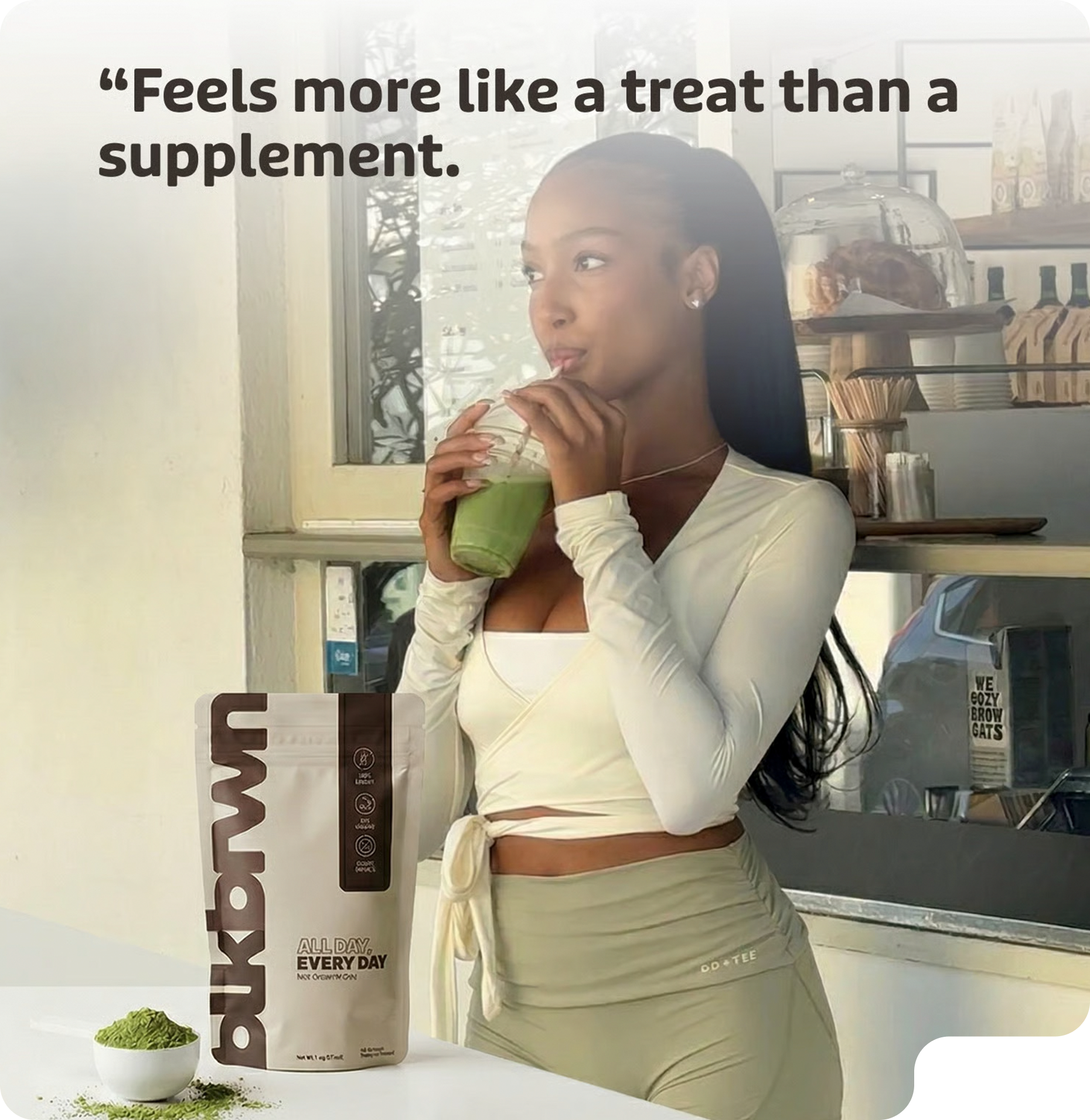 A woman drinks a green beverage, with a pouch and a scoop of green powder on the table.