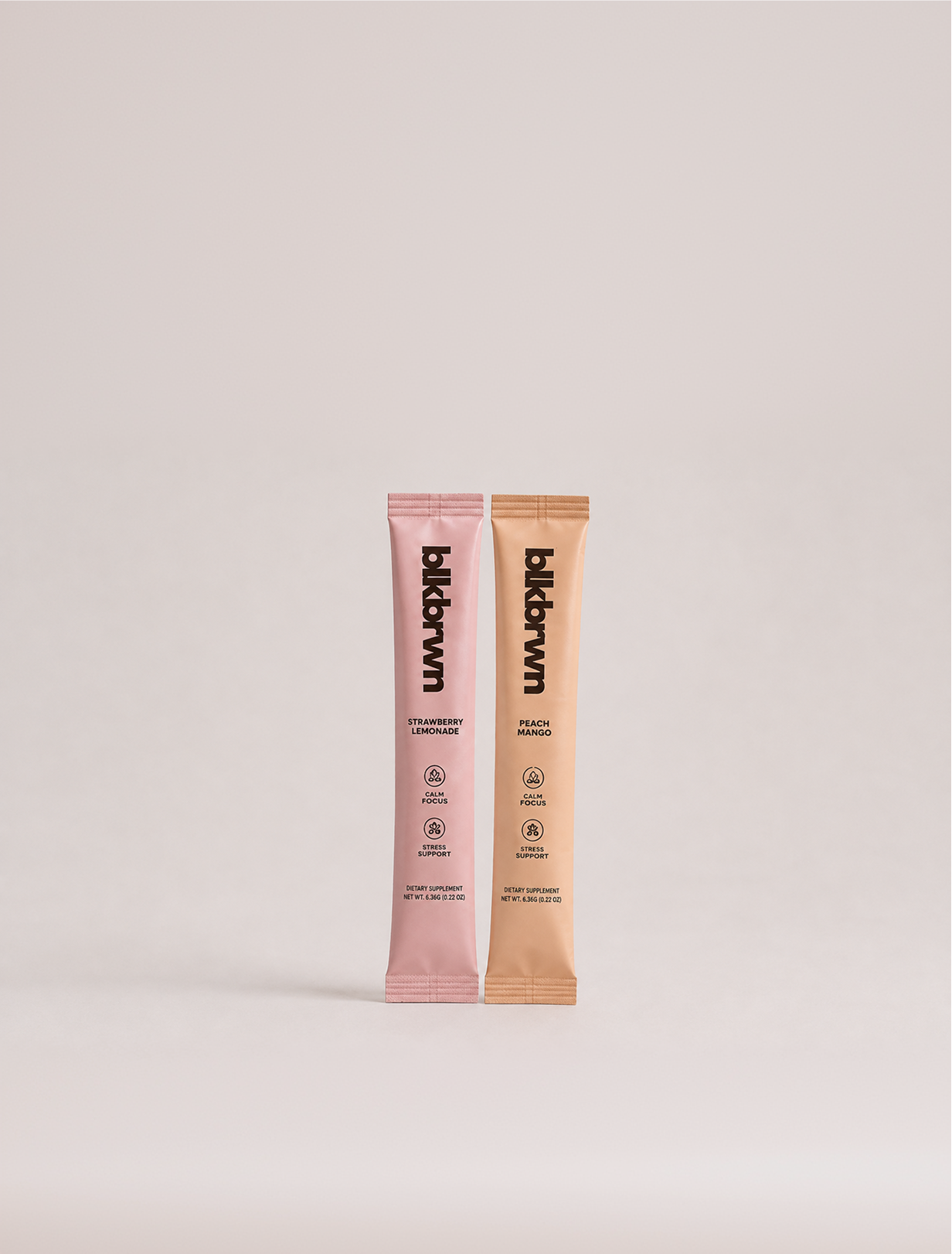 Two single-serving packets of blkbrwn dietary supplement in strawberry lemonade and peach mango flavors against a plain background.