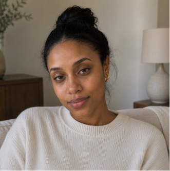 A woman with dark hair in a bun, wearing a cream-colored sweater, looks directly at the camera.