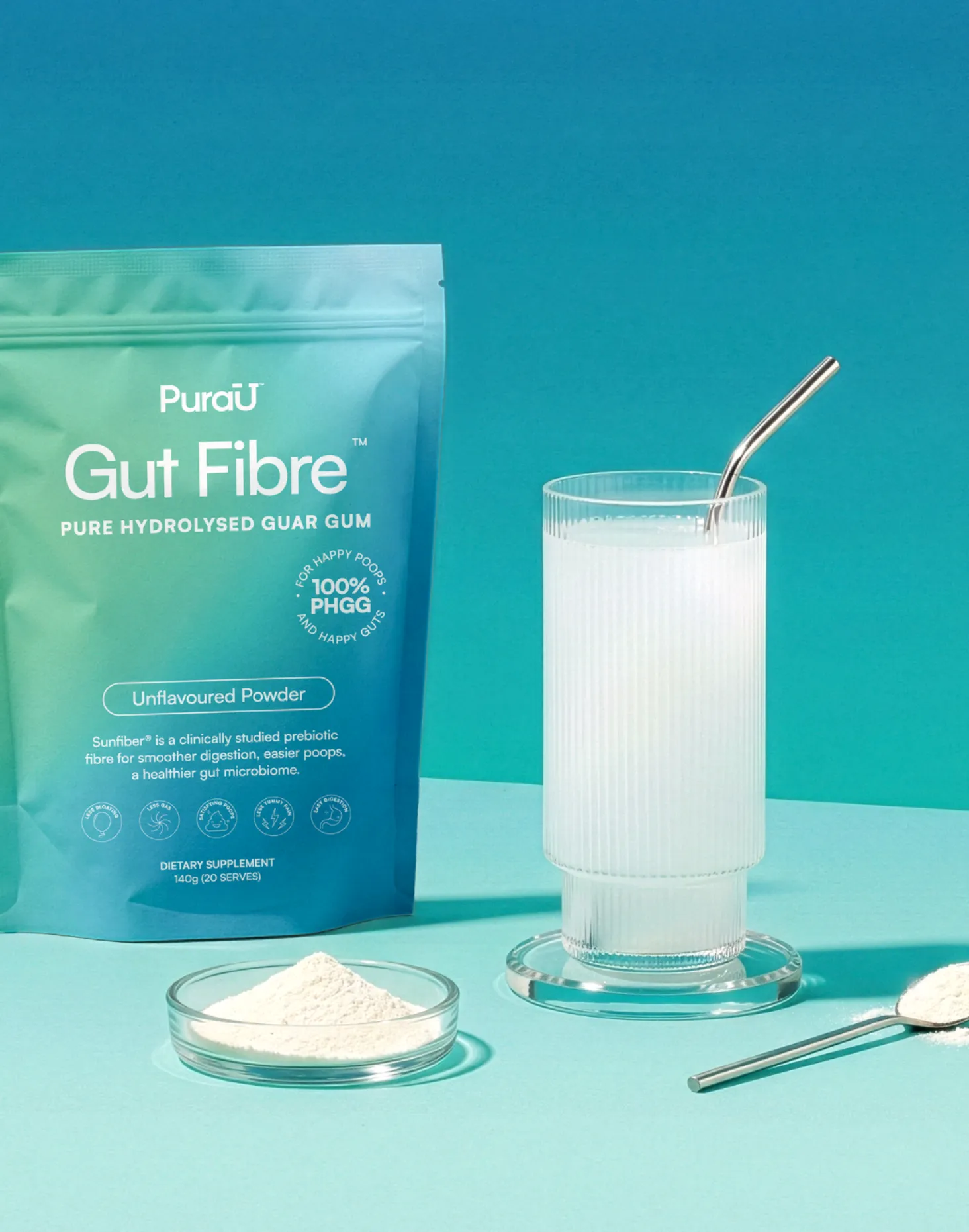 A teal packet of 'Gut Fibre' powder next to a filled glass with a metal straw. A small dish of powder and a spoon are nearby, set against a turquoise background.