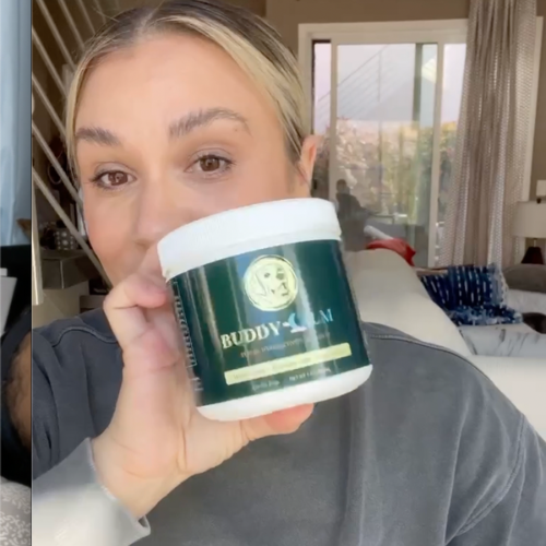 Person holding a jar labeled 'Buddy Balm' in a living room.