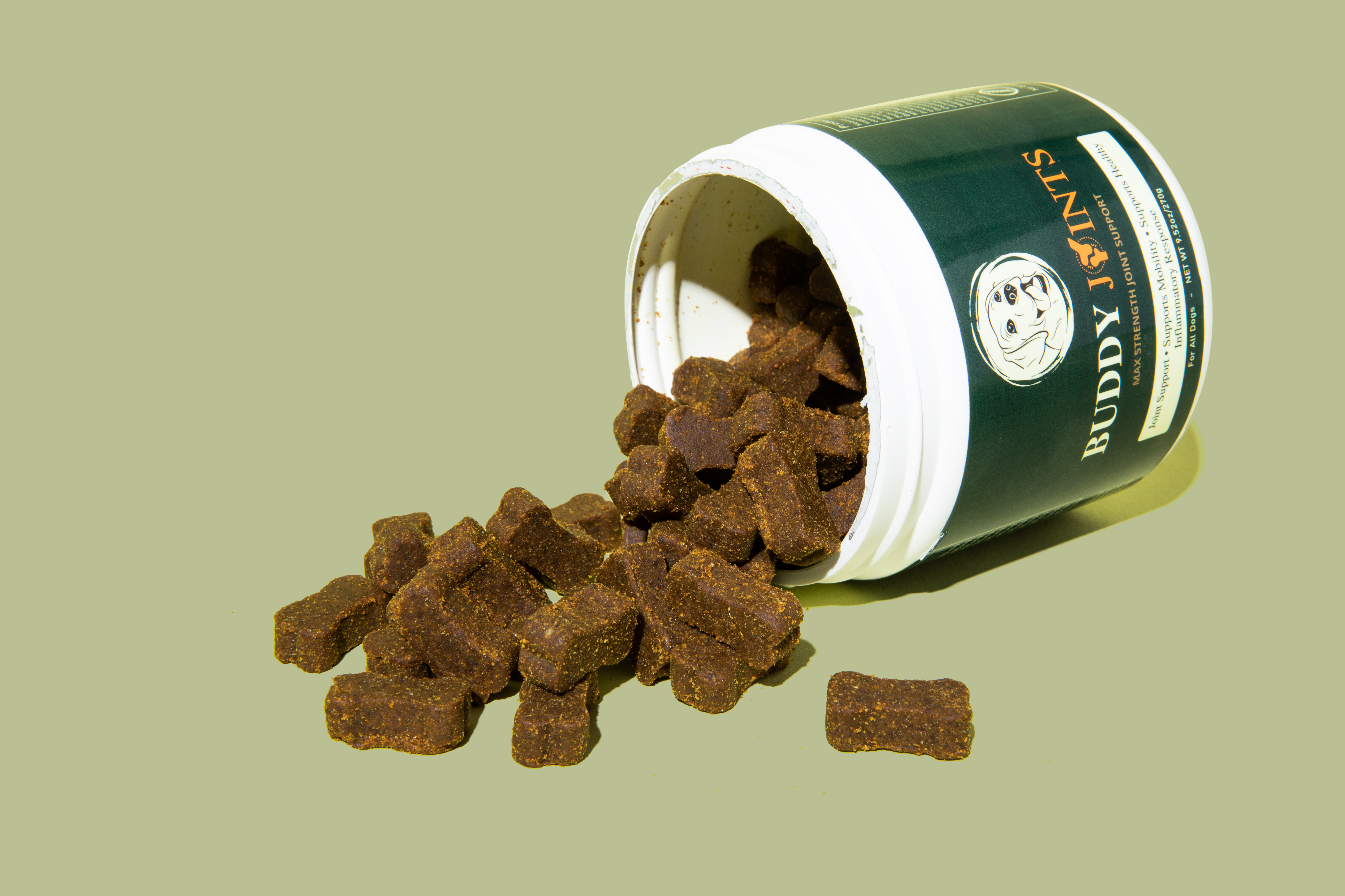 Dog treats spilling from a container labeled 'Buddy Joints' on a green background.