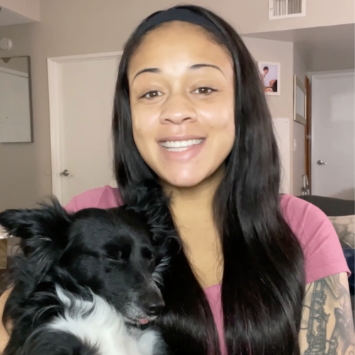 Person smiling while holding a black and white dog indoors.