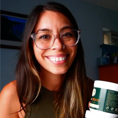 Smiling person with glasses holding a container indoors.