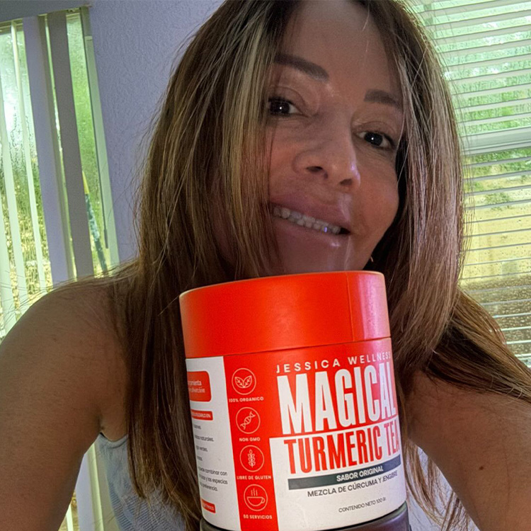 A smiling woman with long highlighted hair holds up an orange container of Magical Turmeric Tea.