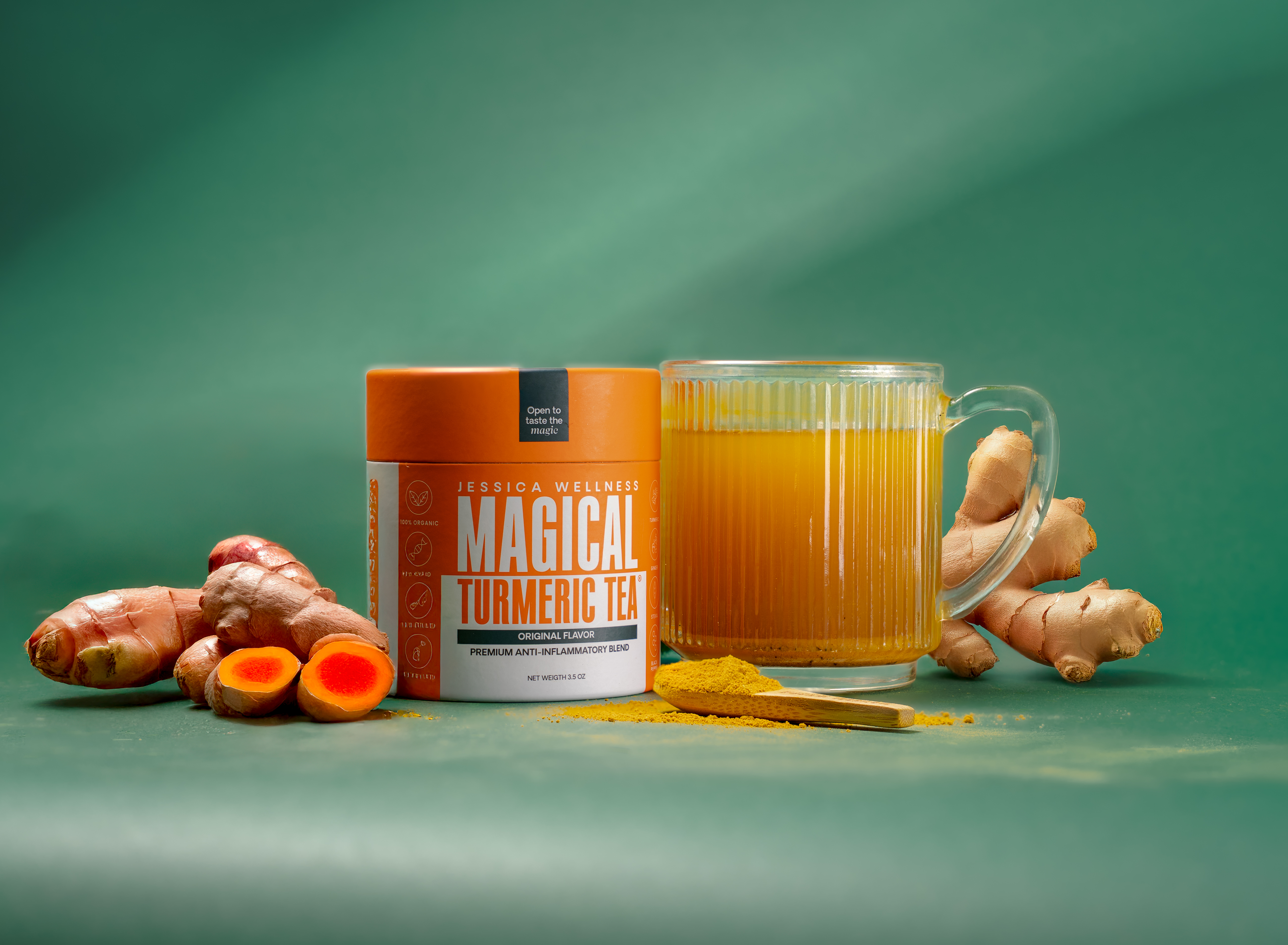A container of turmeric tea next to a glass mug of tea, fresh turmeric, and ginger root.