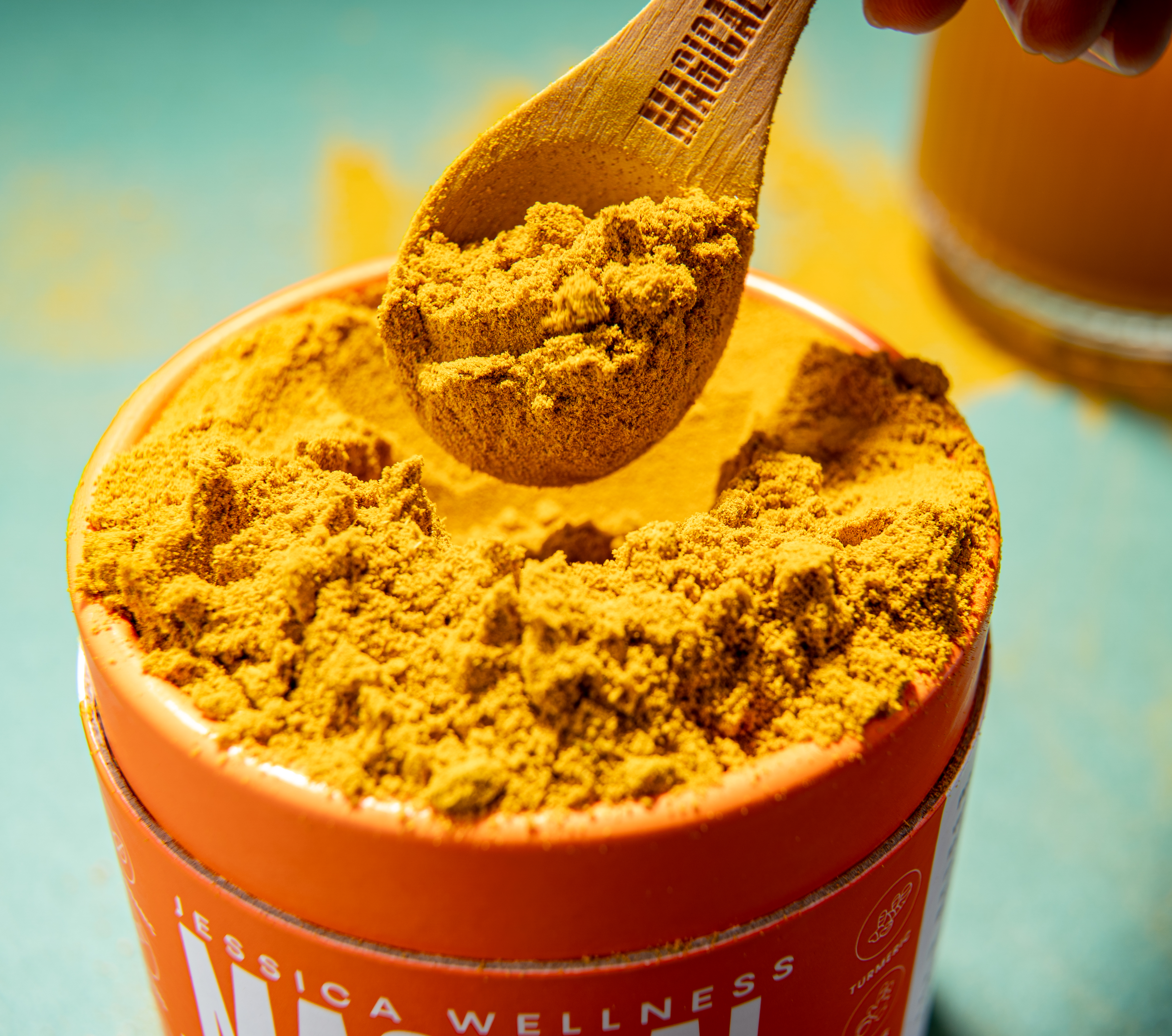 A close-up of a wooden spoon scooping yellow turmeric powder out of an orange container.
