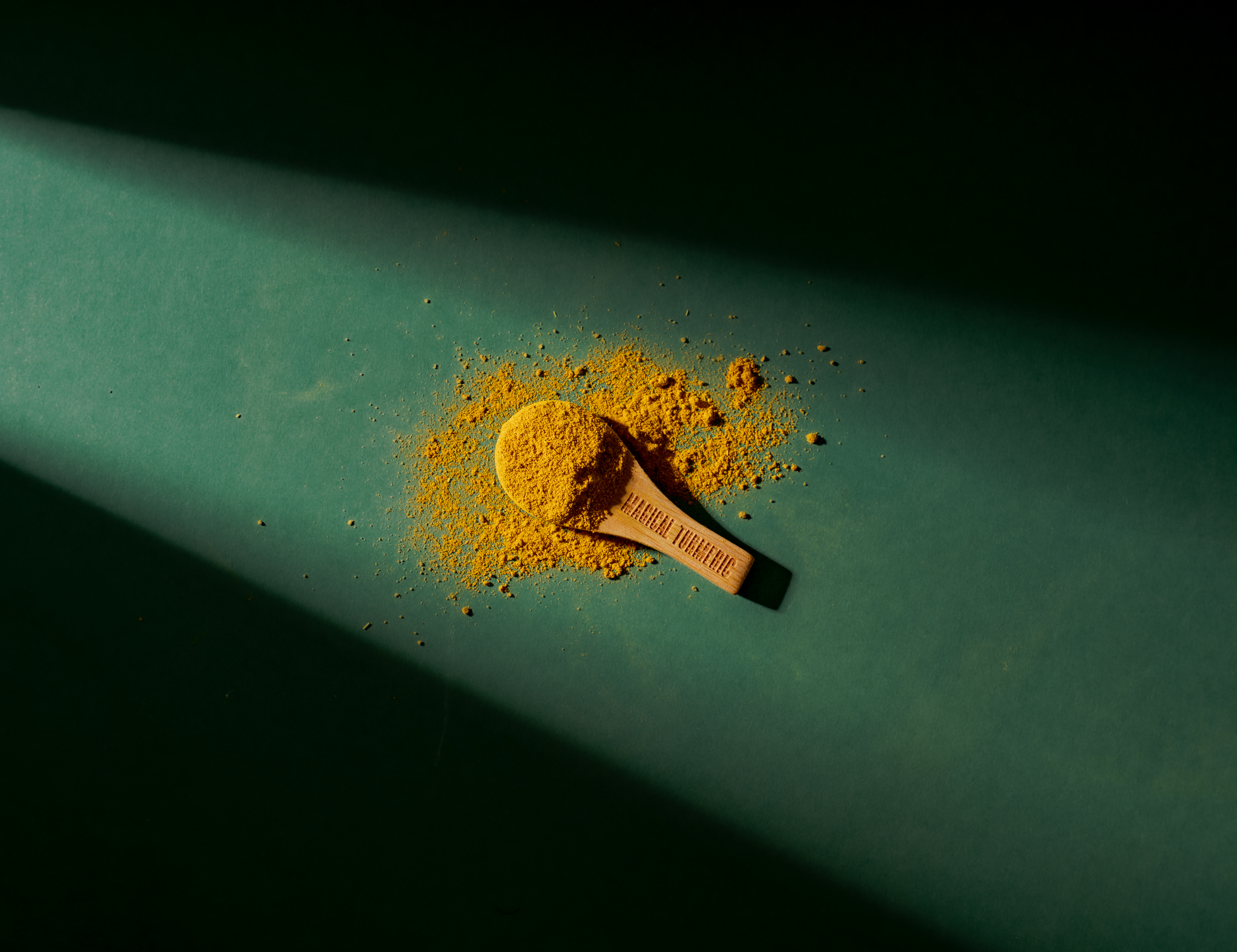A wooden spoon filled with yellow turmeric powder on a dark green background, with dramatic lighting.