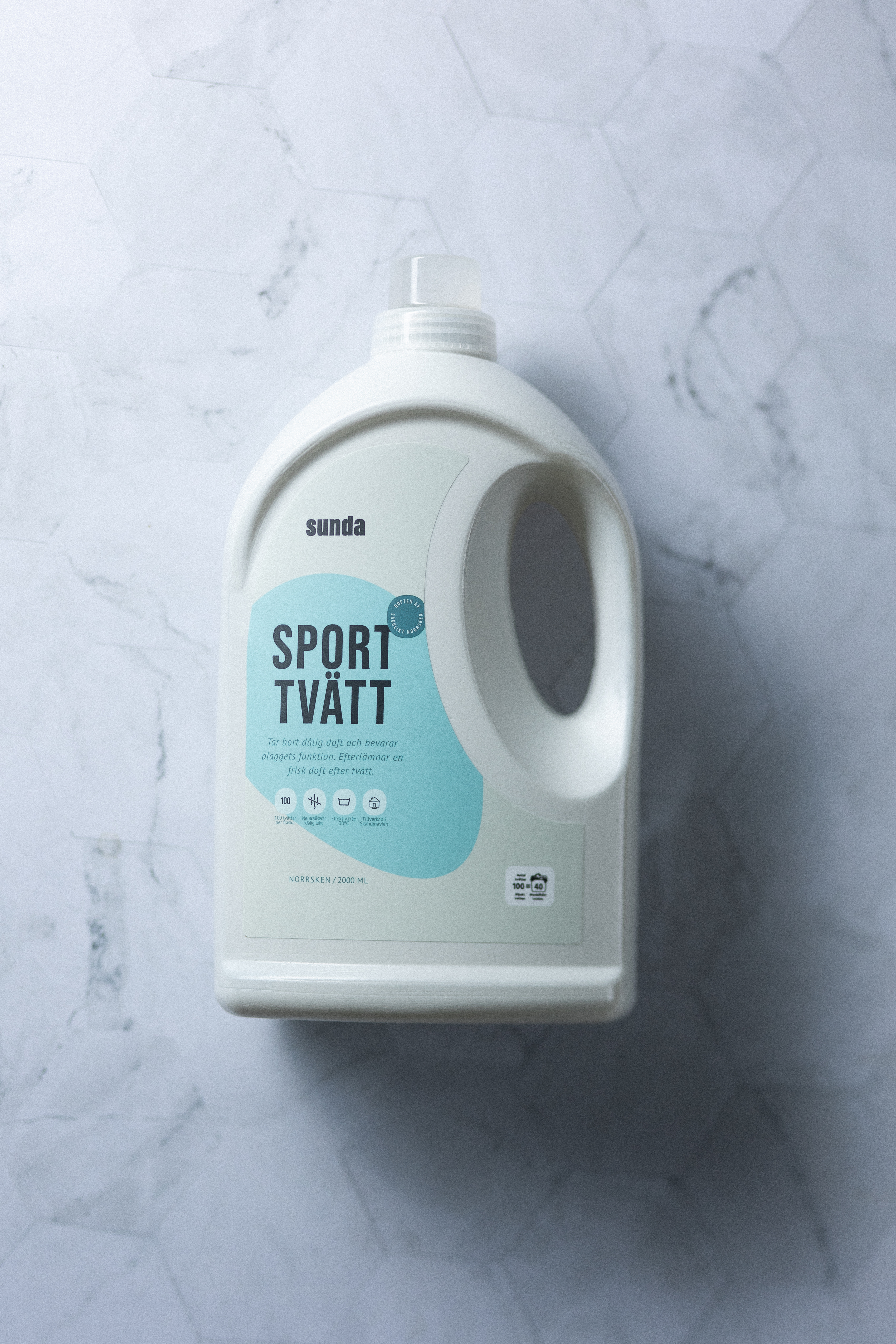 White bottle of 'Sport Tvätt' detergent on a marble surface.