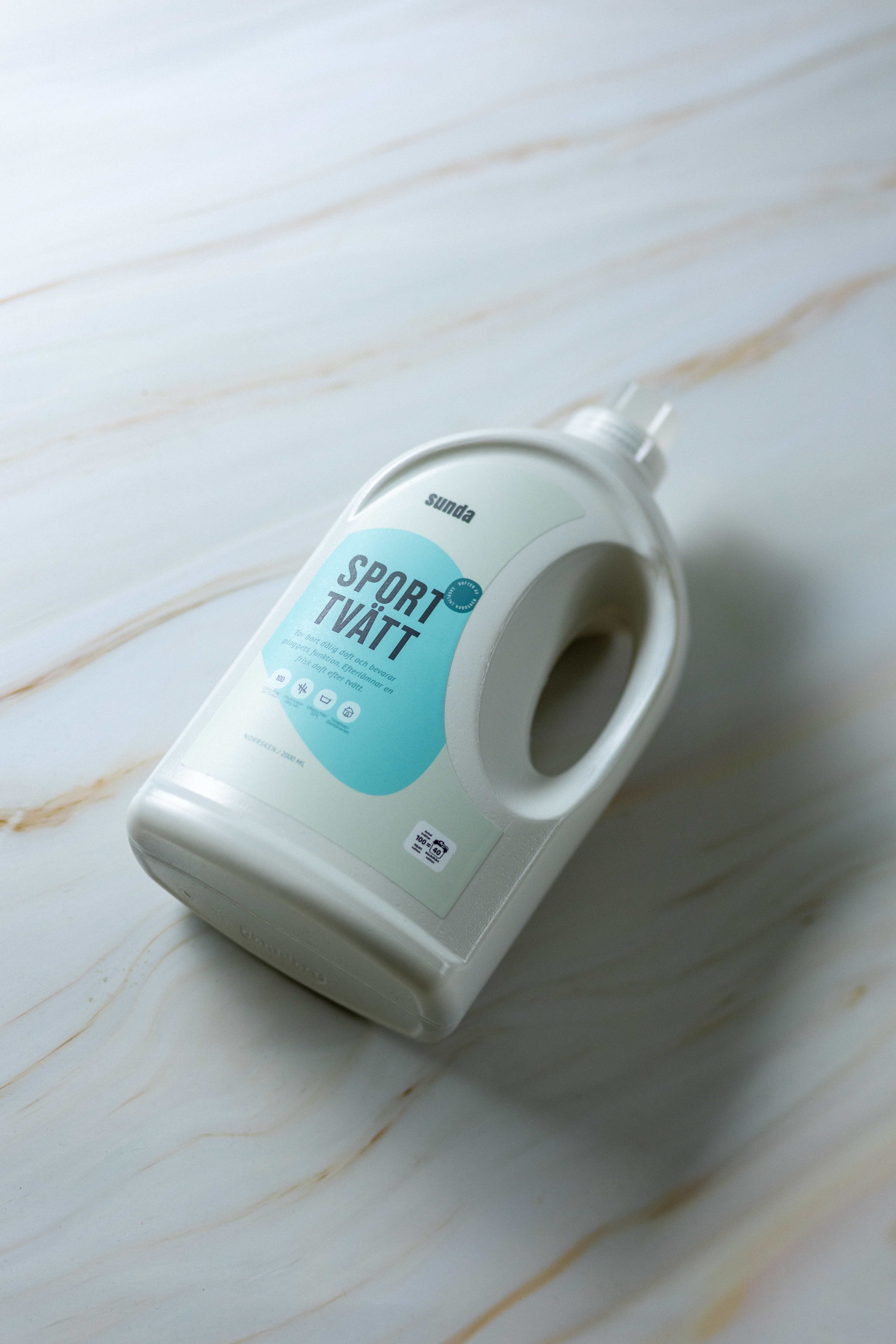 White bottle of laundry detergent labeled 'Sport Tvätt' on a marble surface.