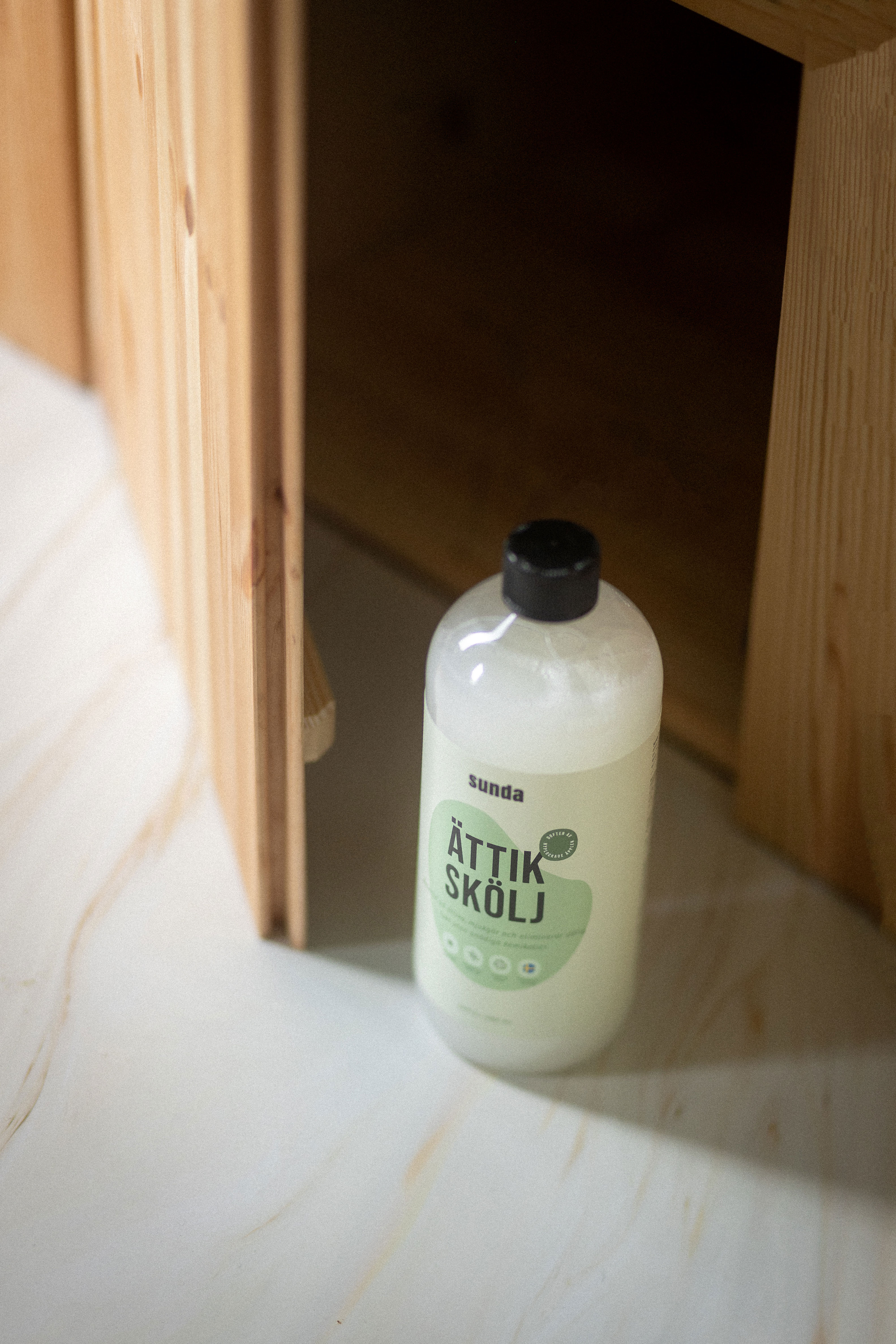 Bottle of cleaning product on a light wooden floor near a cabinet.