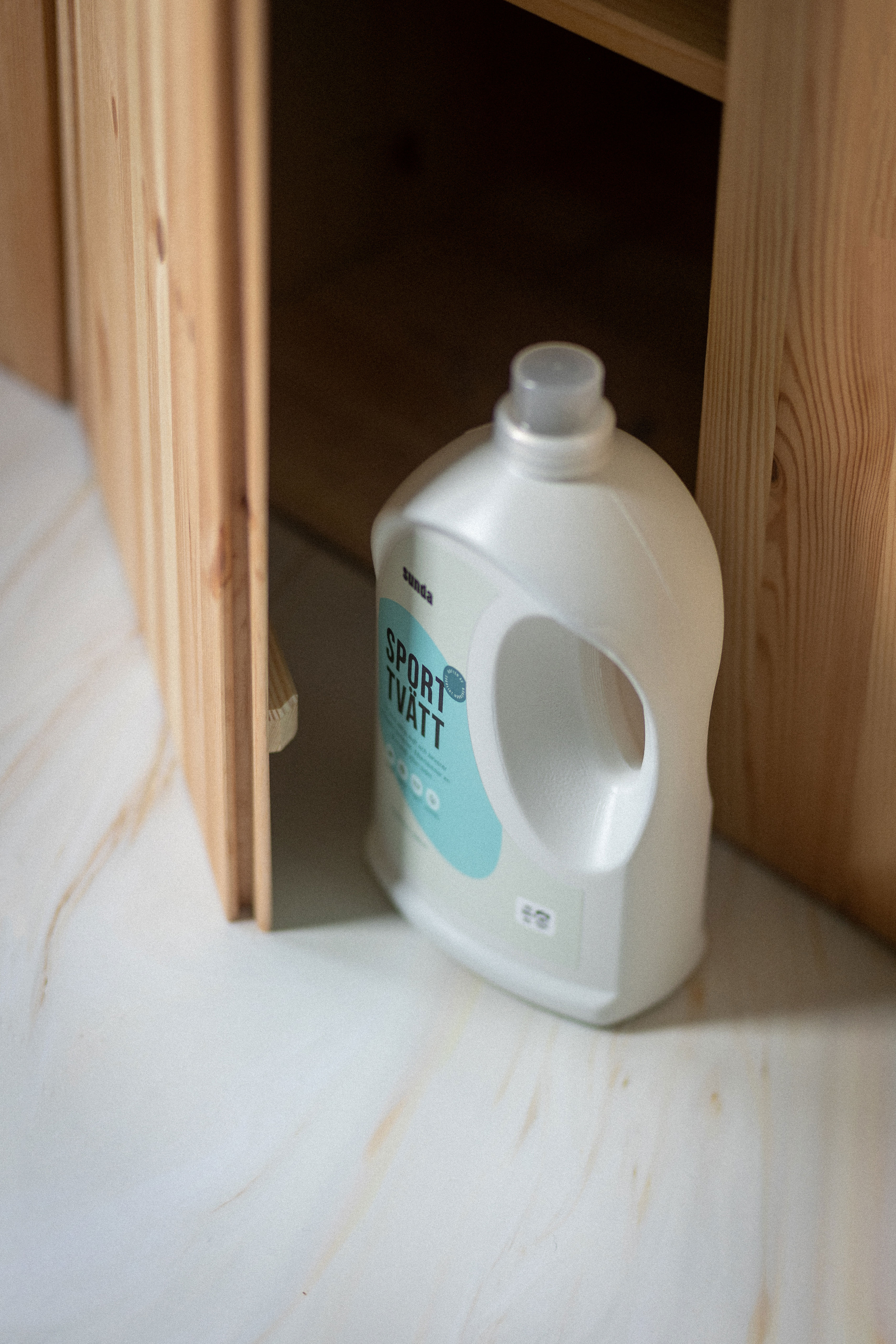 White detergent bottle labeled 'Sport Tvätt' beside a wooden cabinet.