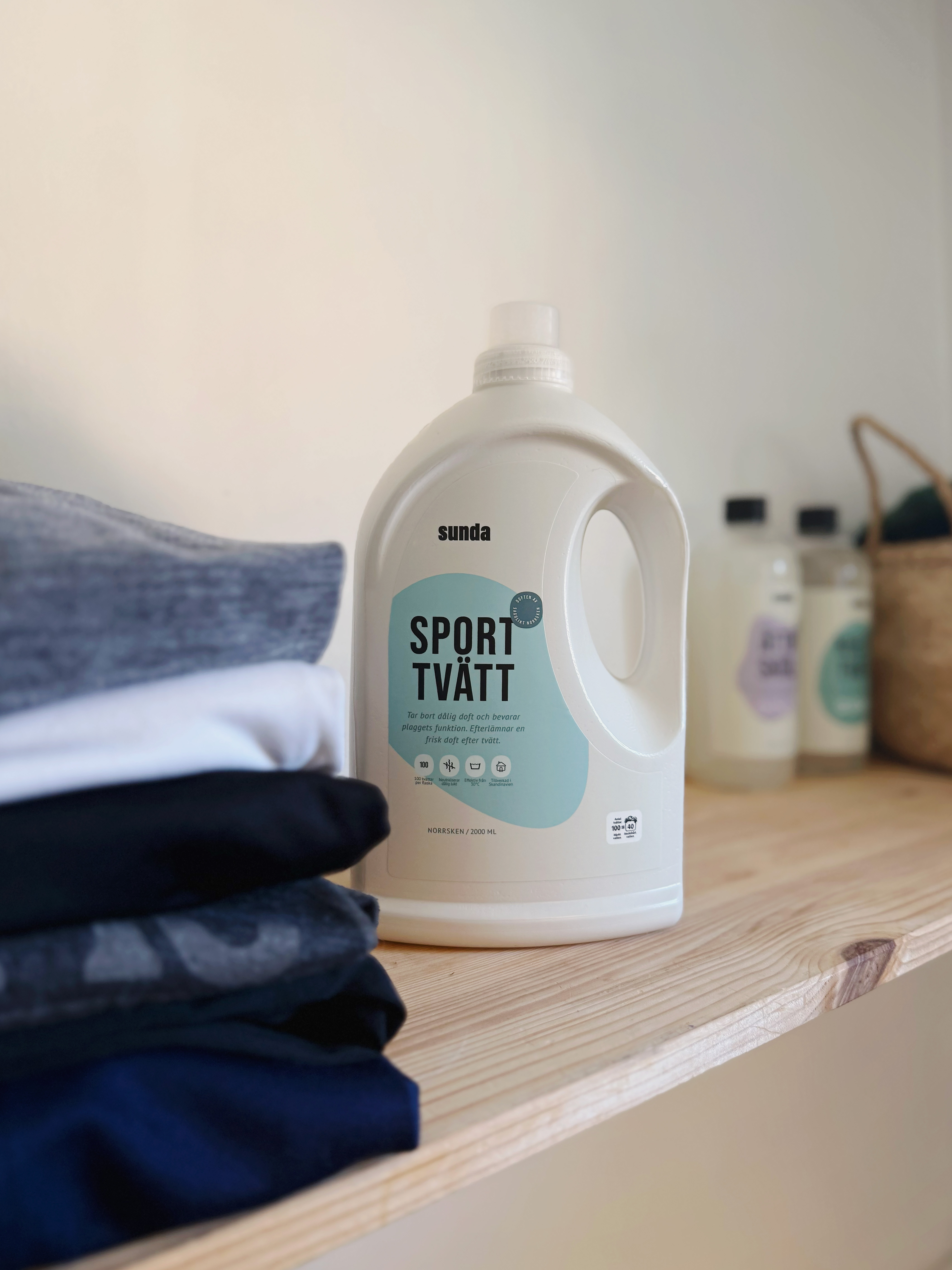 Laundry detergent bottle on a wooden shelf with folded clothes.