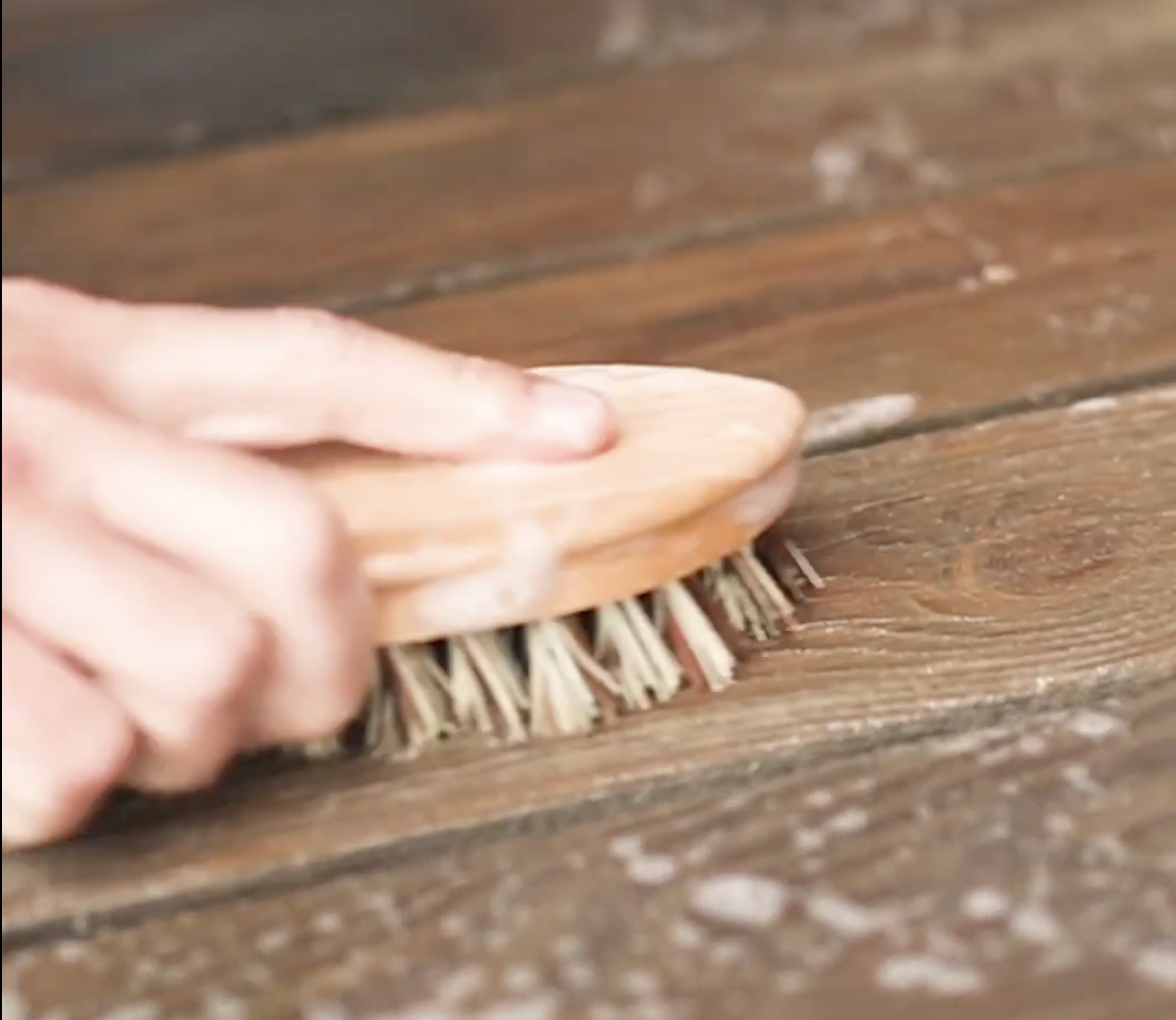 Hand scrubbing a wooden surface with a brush.