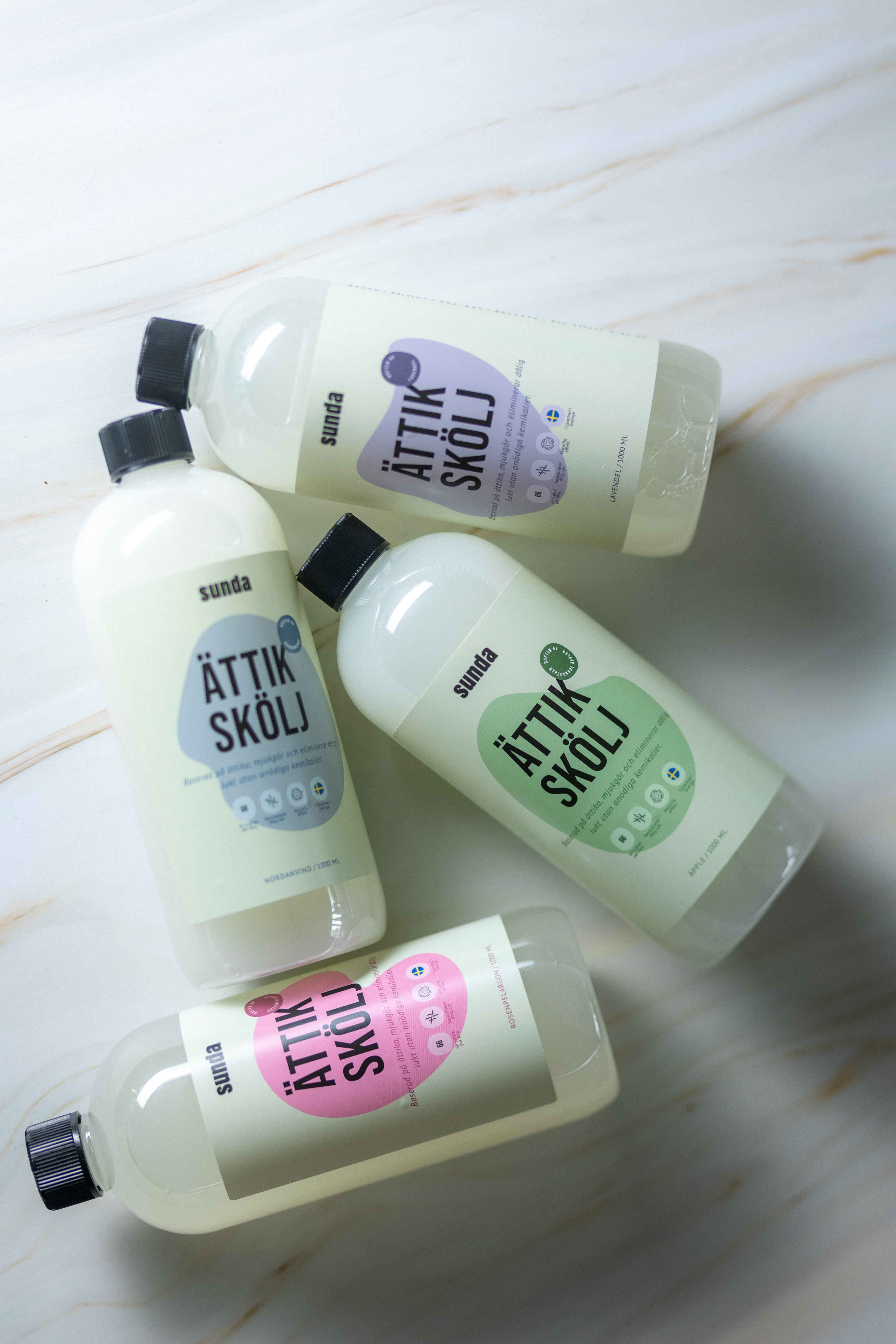 Four bottles of 'Ättik Skölj' with different colored labels on a marble surface.